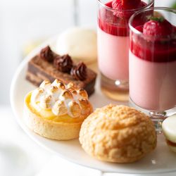 Assorted French pastries and desserts on a white platter including tart, choux pastry, macaron, brownie, and raspberry mousse.