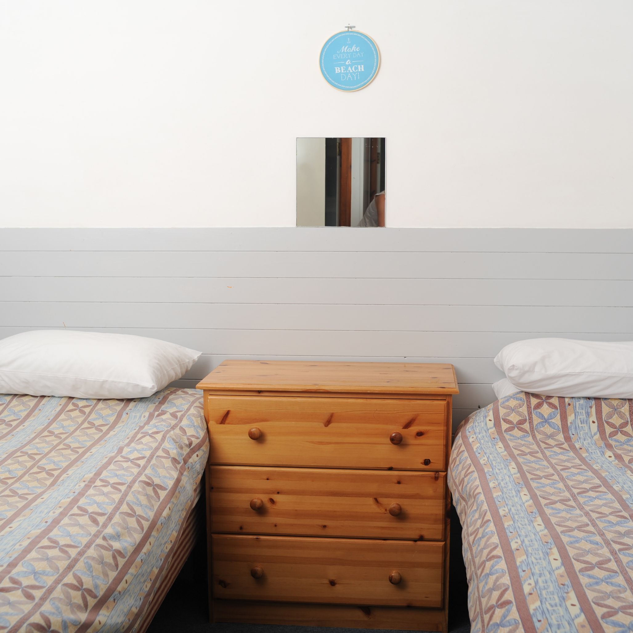 A simple bedroom with two single beds and a wooden dresser between them.