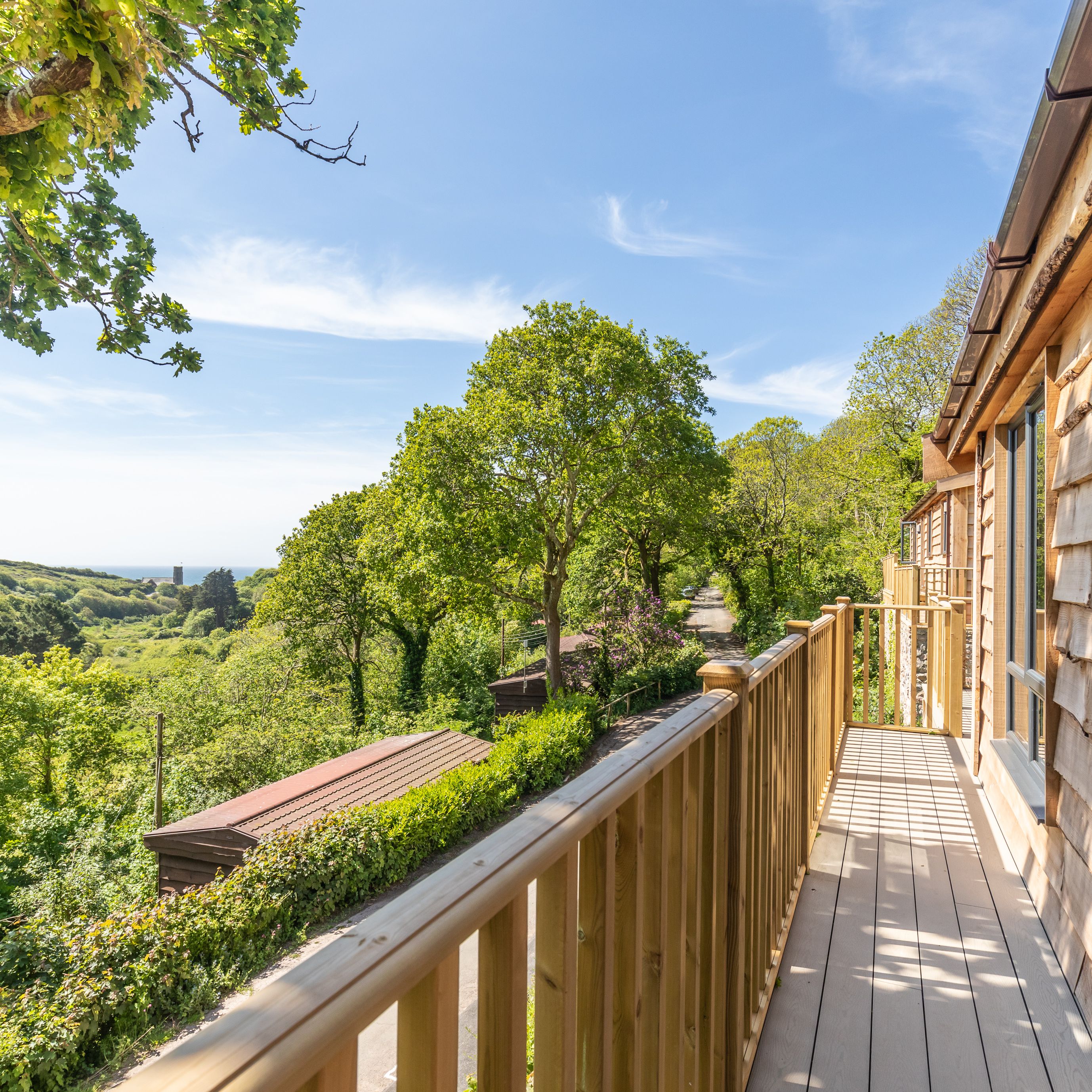 Wooden balcony overlooking lush green trees and distant hills under a blue sky
