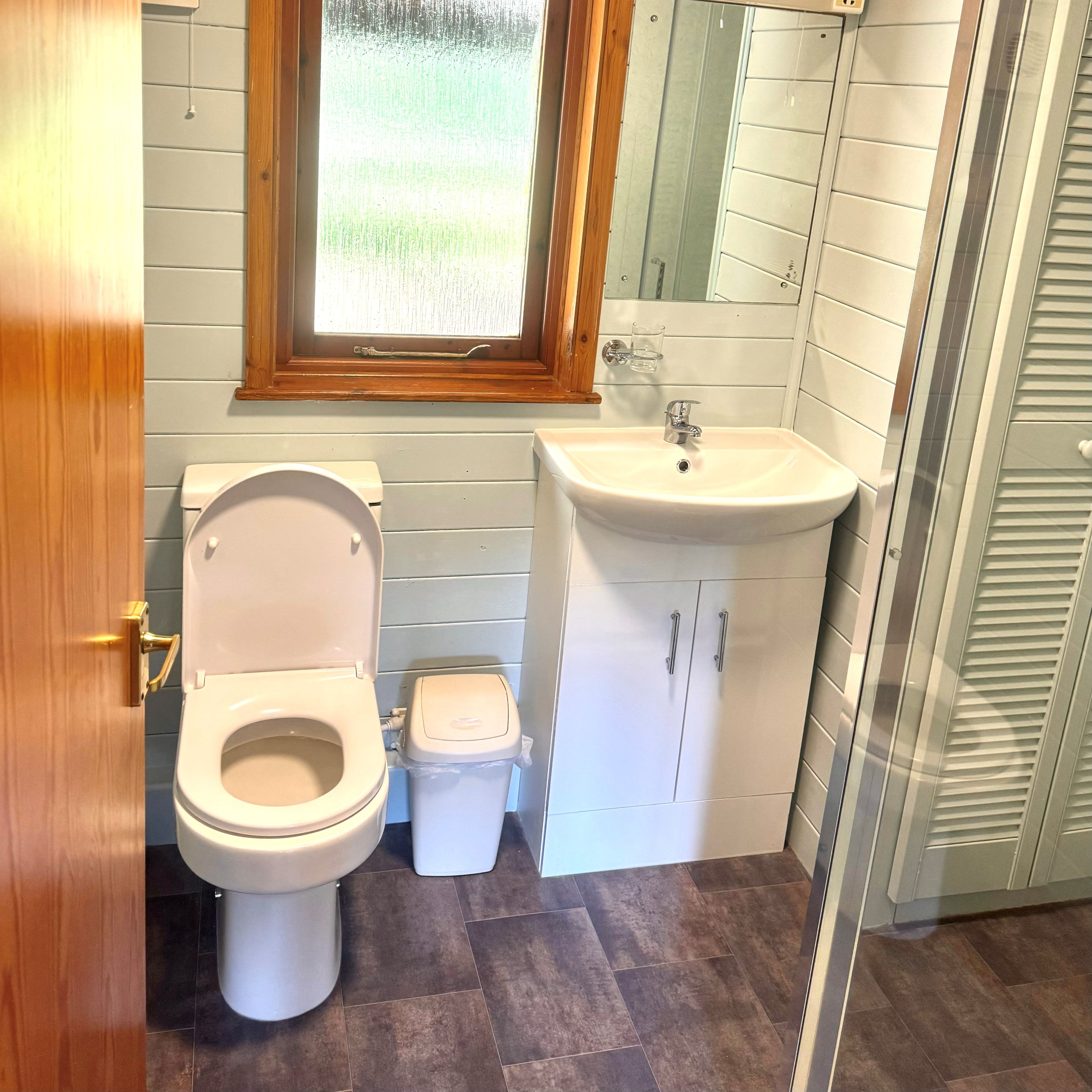 Small bathroom with wooden ceiling, toilet, sink, and shower