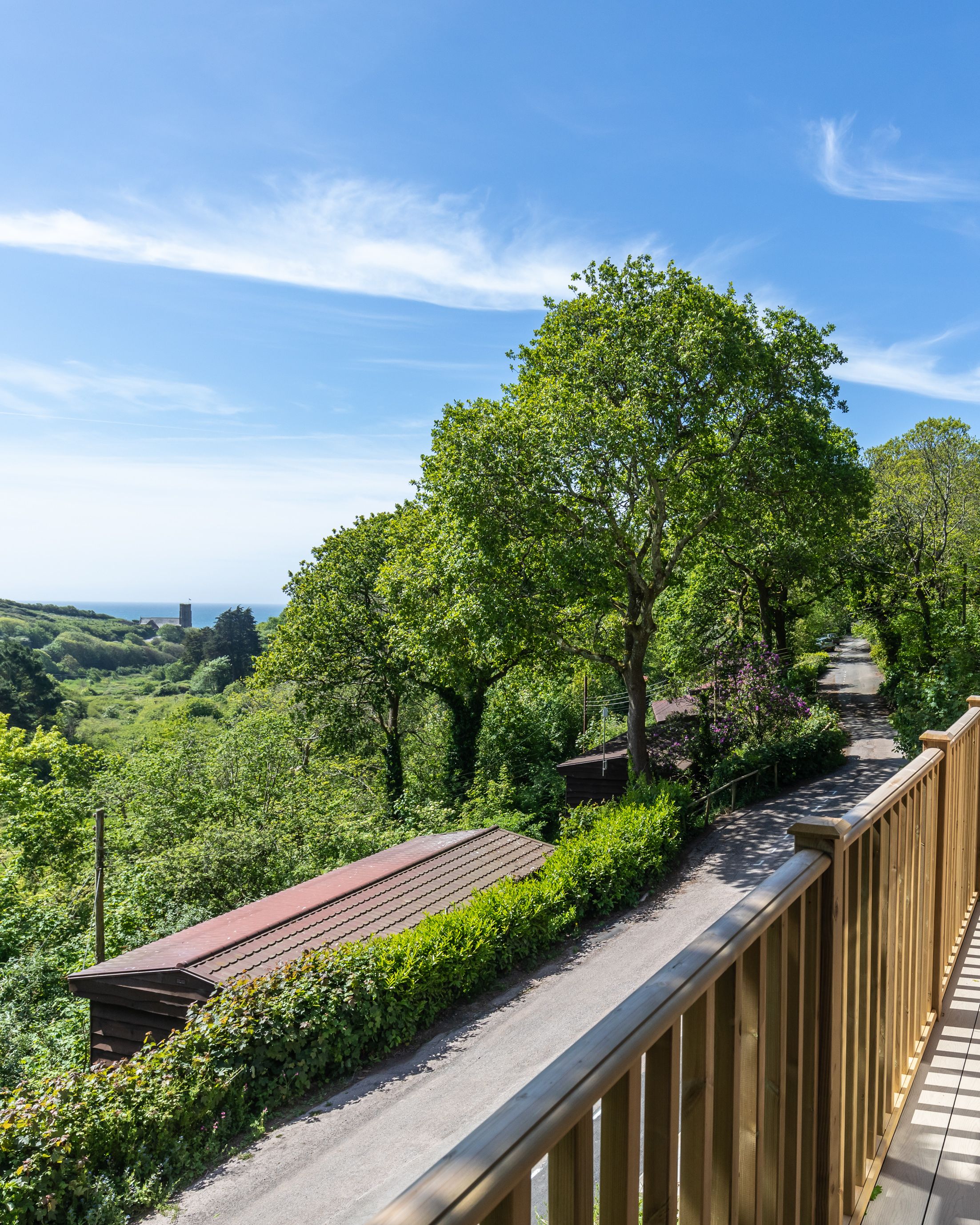 Wooden balcony overlooking a lush green landscape with trees and a clear blue sky.