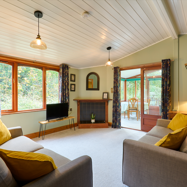 Cozy living room with grey sofas, yellow cushions, large window, fireplace, and a view into a sunroom.