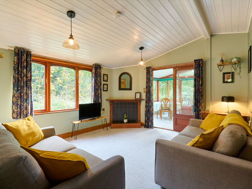 Cozy living room with grey sofas, yellow cushions, large window, fireplace, and a view into a sunroom.