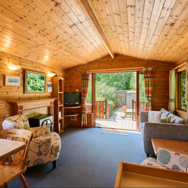 Cozy wooden cabin interior with large windows and an open door to a deck.