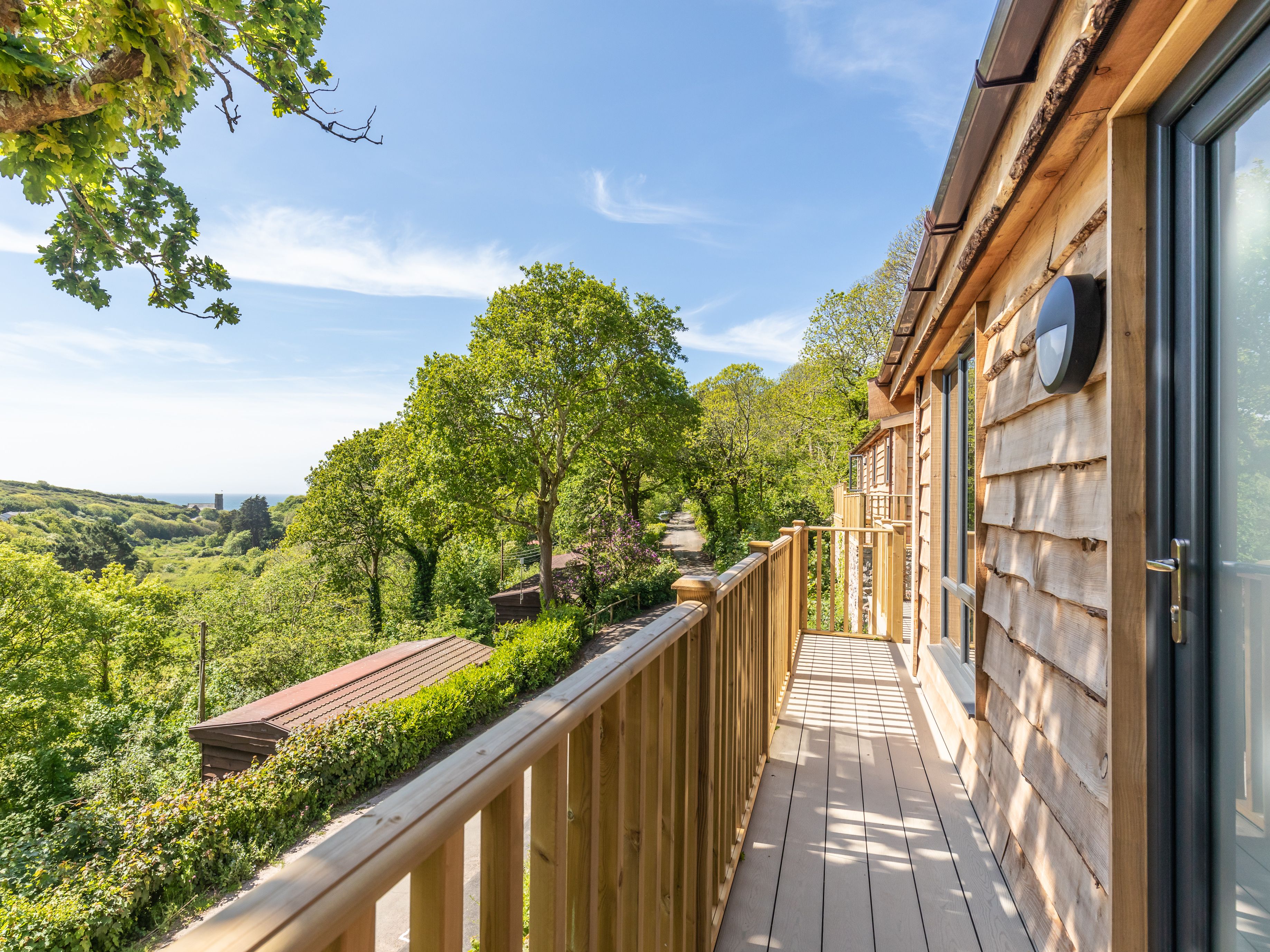 Wooden balcony overlooking lush green trees and a scenic countryside view.