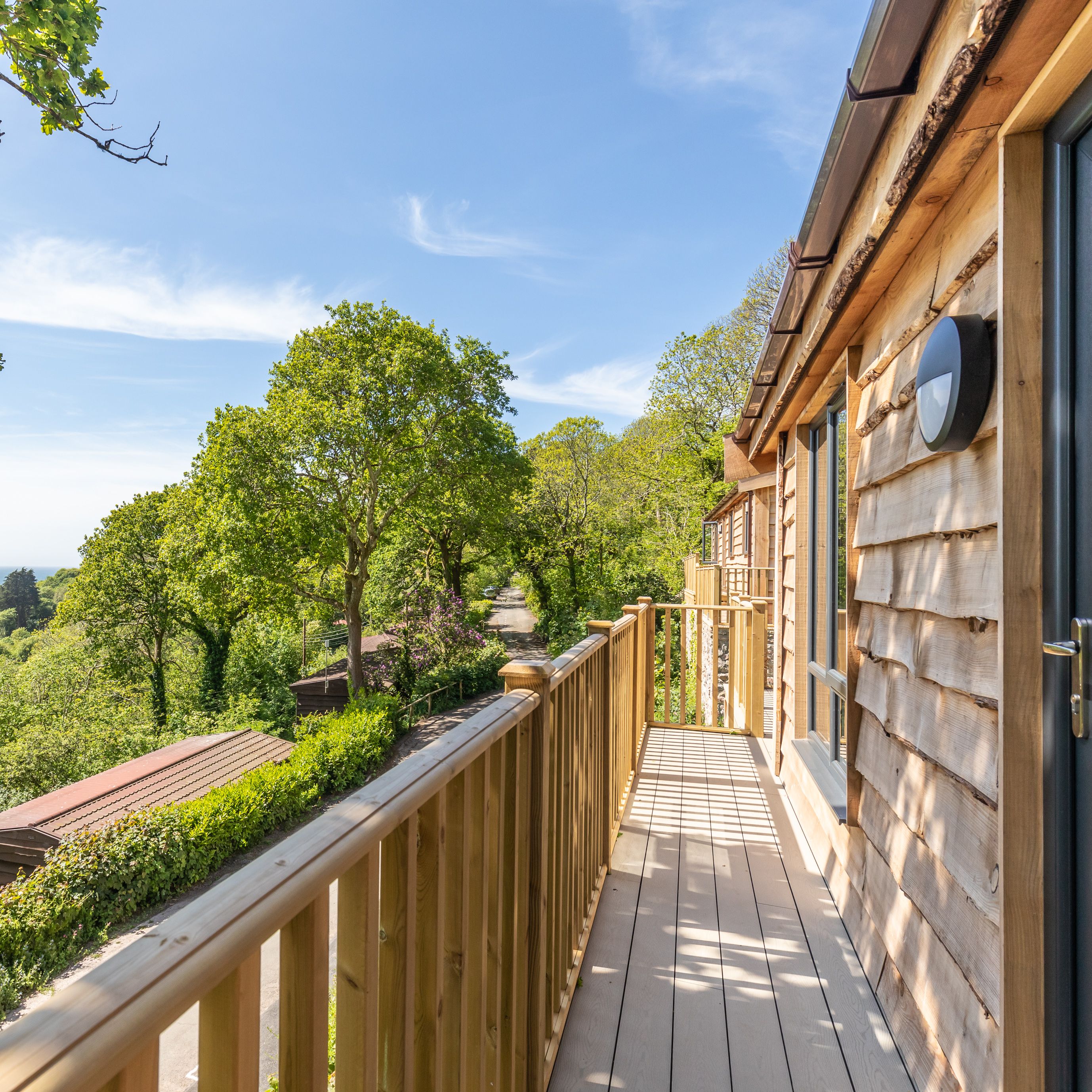 Wooden balcony overlooking lush green trees and a scenic countryside view.