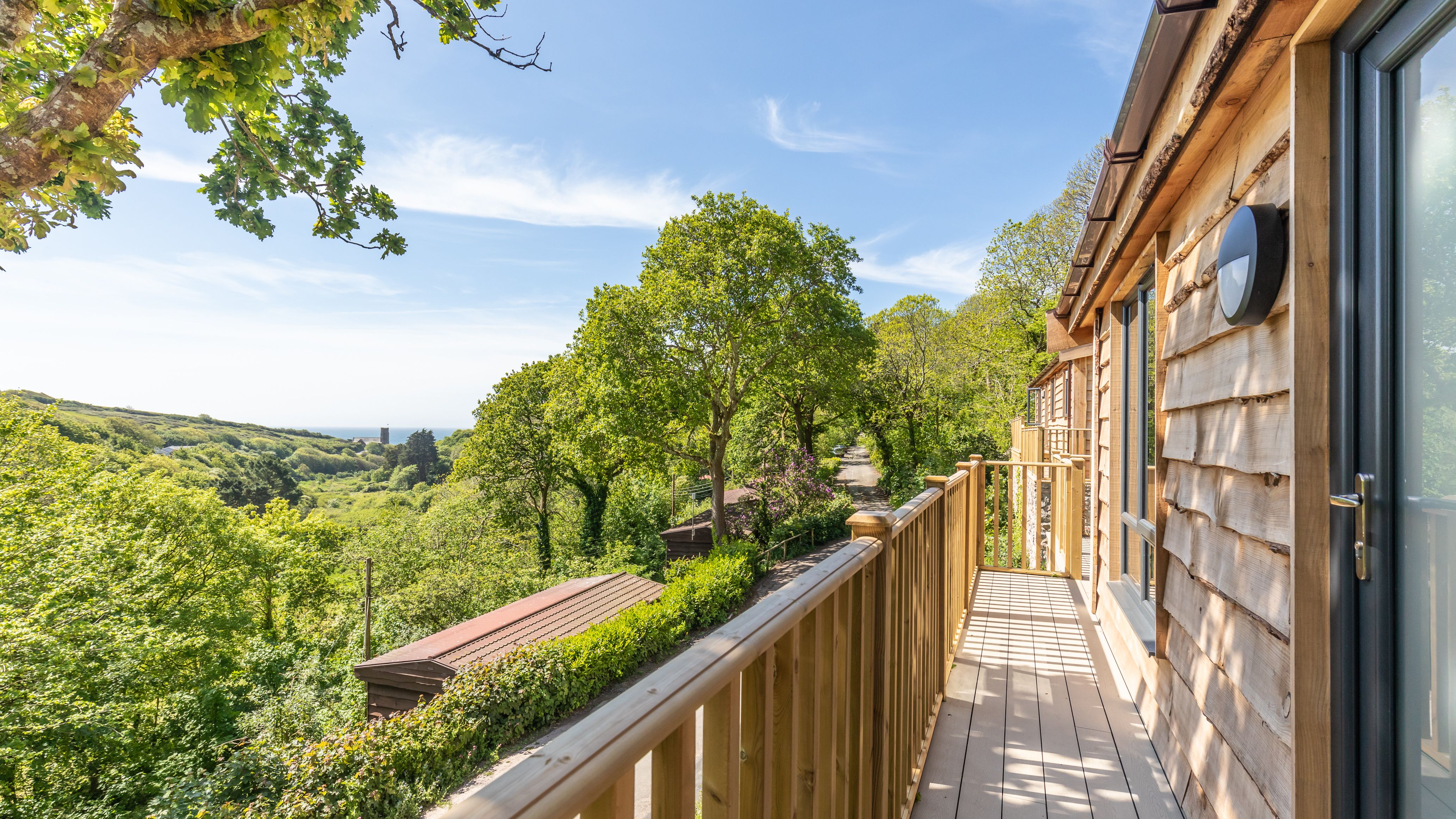 Wooden balcony overlooking lush green trees and a scenic countryside view.