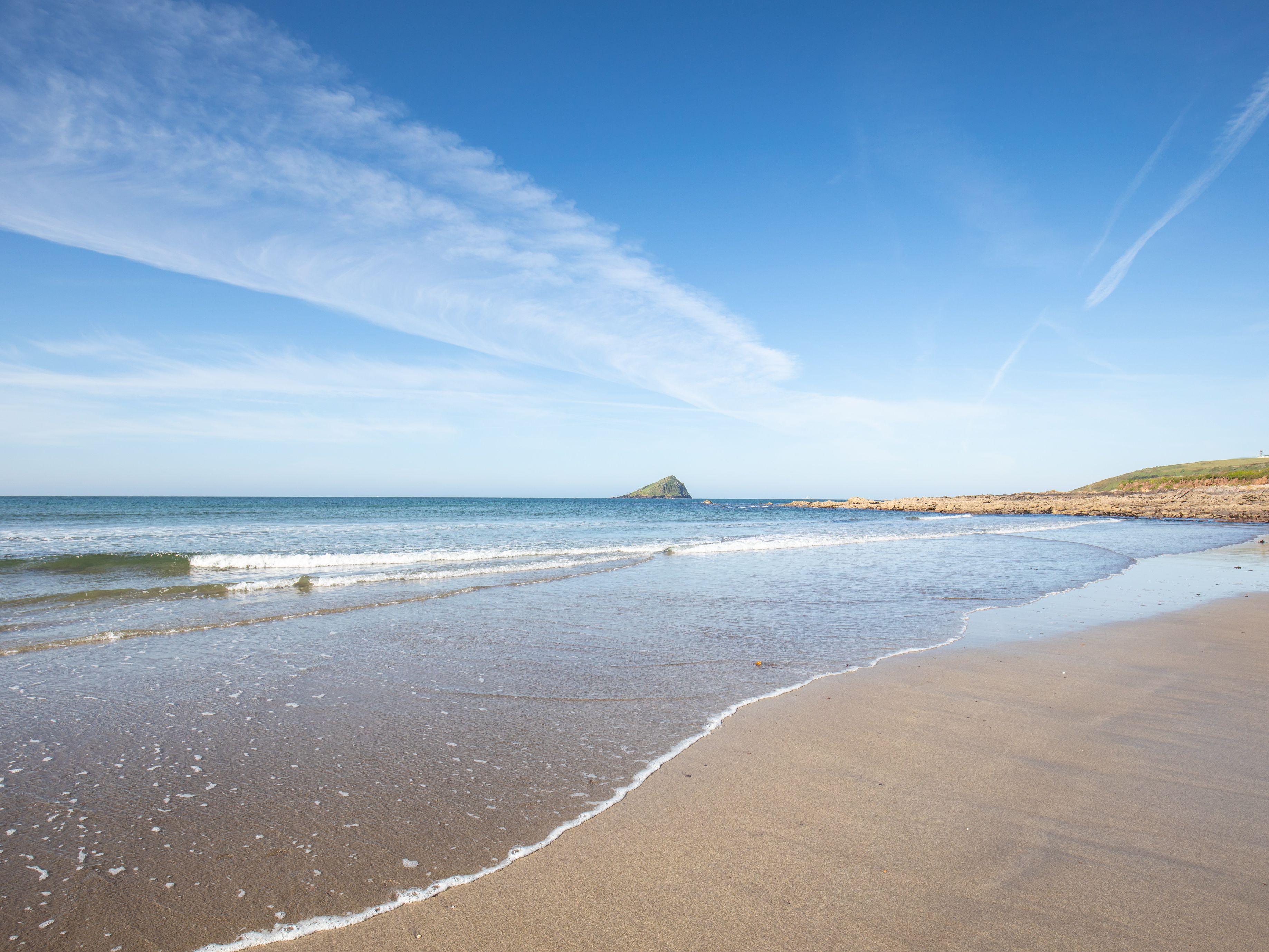 Sandy beach with gentle waves, blue sky, and a small island in the distance