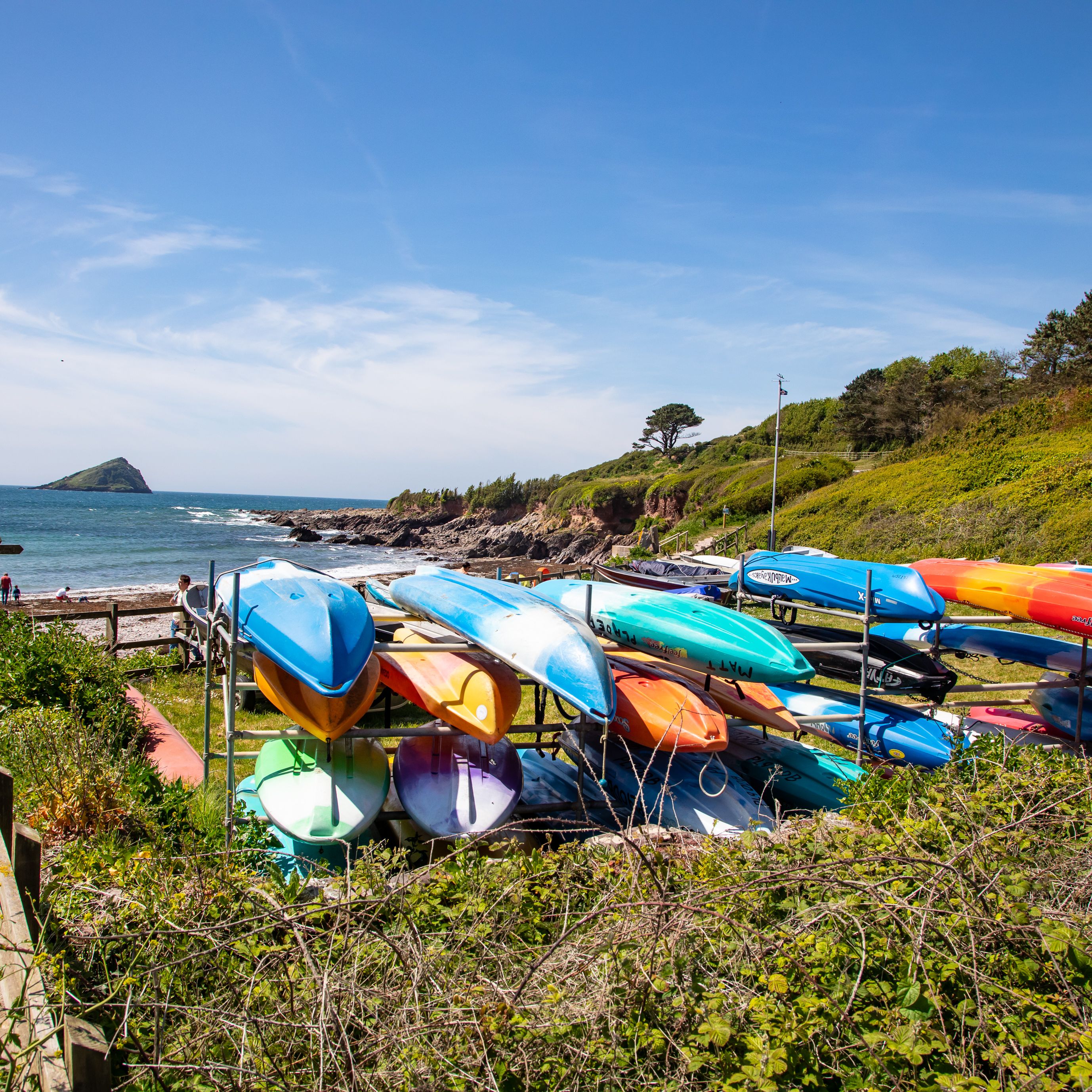 Colorful kayaks stacked on racks near a beach with a scenic coastline and island in the background.