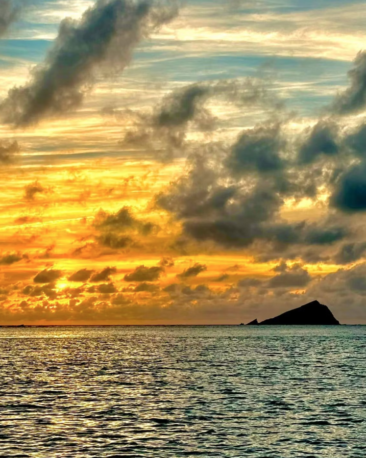 Golden sunset over a calm sea with dramatic clouds and distant island silhouettes
