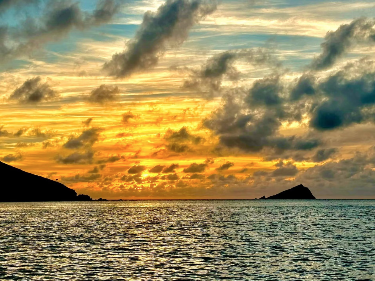 Golden sunset over a calm sea with dramatic clouds and distant island silhouettes
