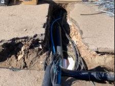 Electrician wiring cables at a distribution point beside a trench