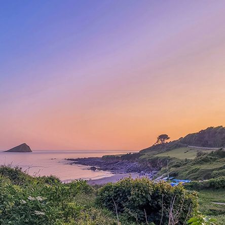 Wembury Beach landscape at sunset with pastel-colored sky and a distant island.
