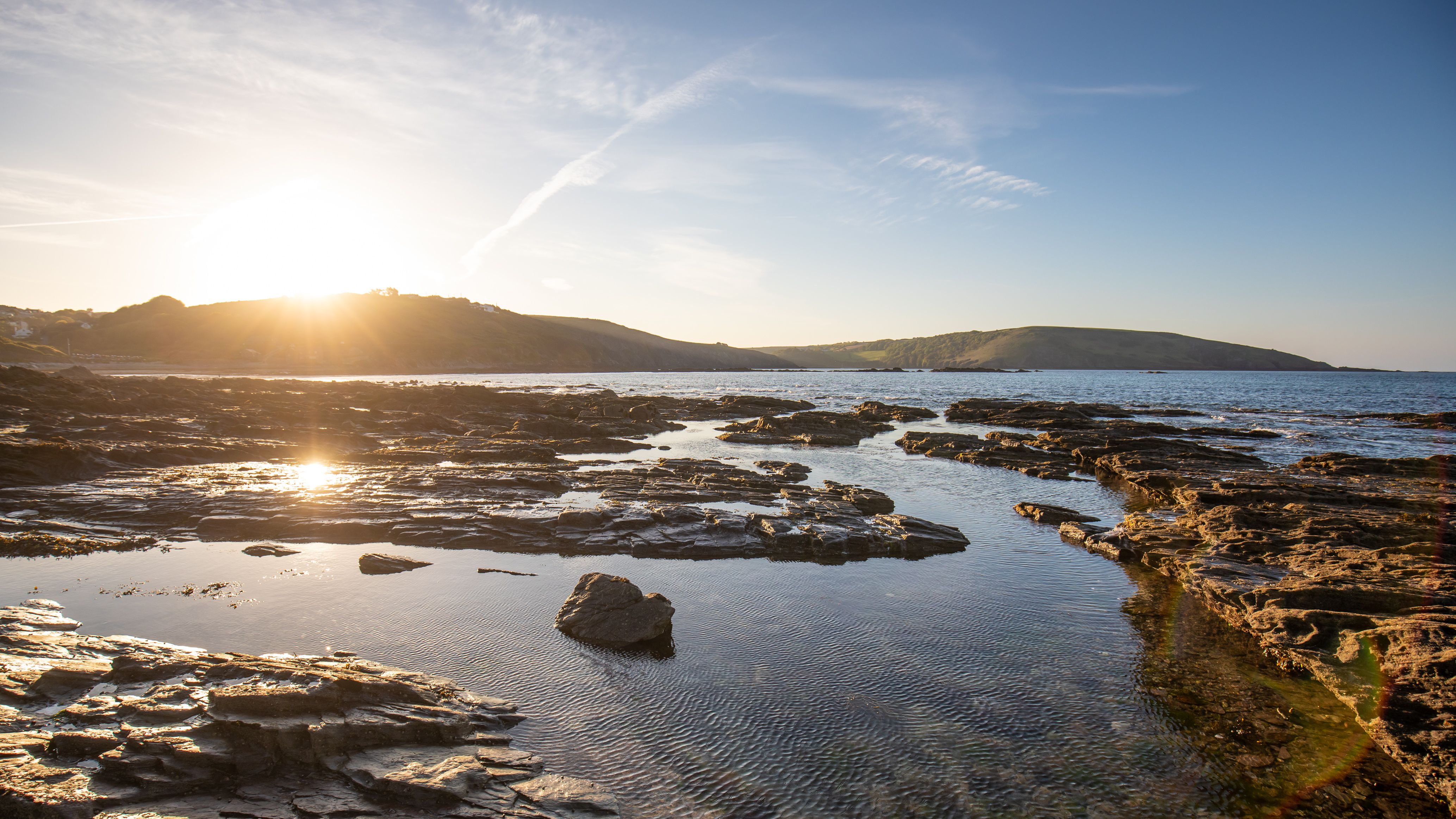 Rocky coastline at sunset with calm waters and distant hills