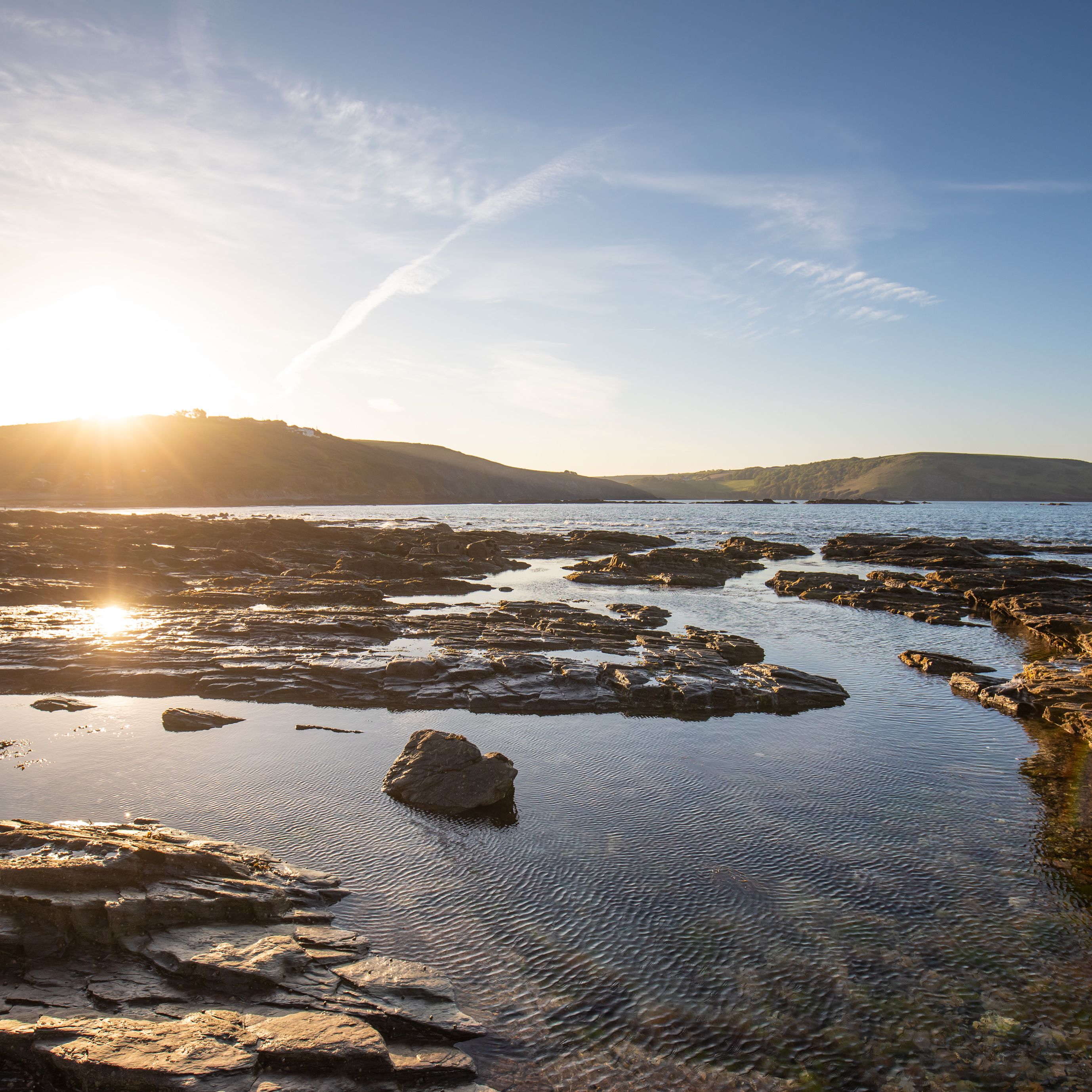Rocky coastline at sunset with calm waters and distant hills
