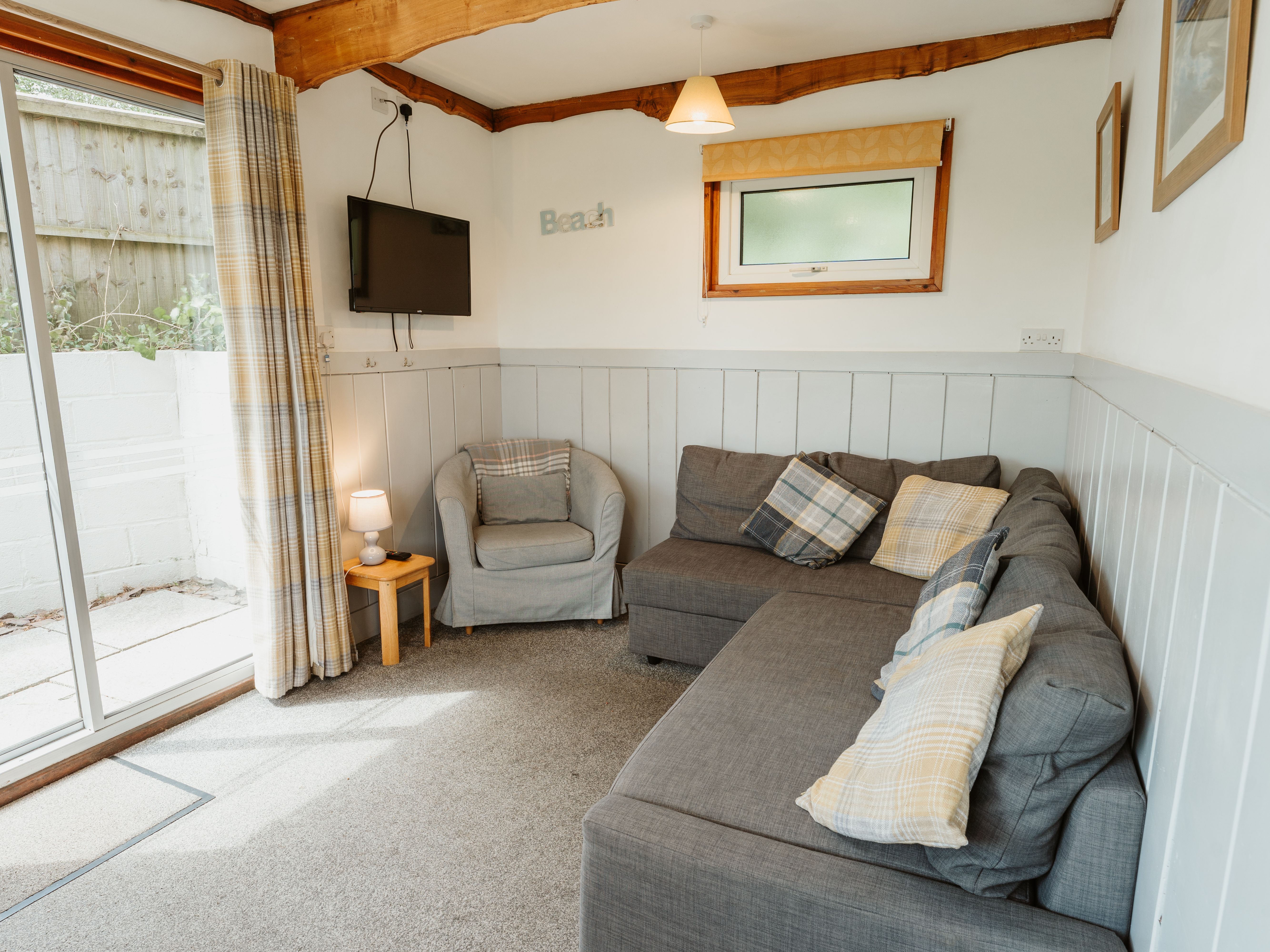 Cosy living area with grey corner sofa, armchair, wall-mounted TV and sliding patio door
