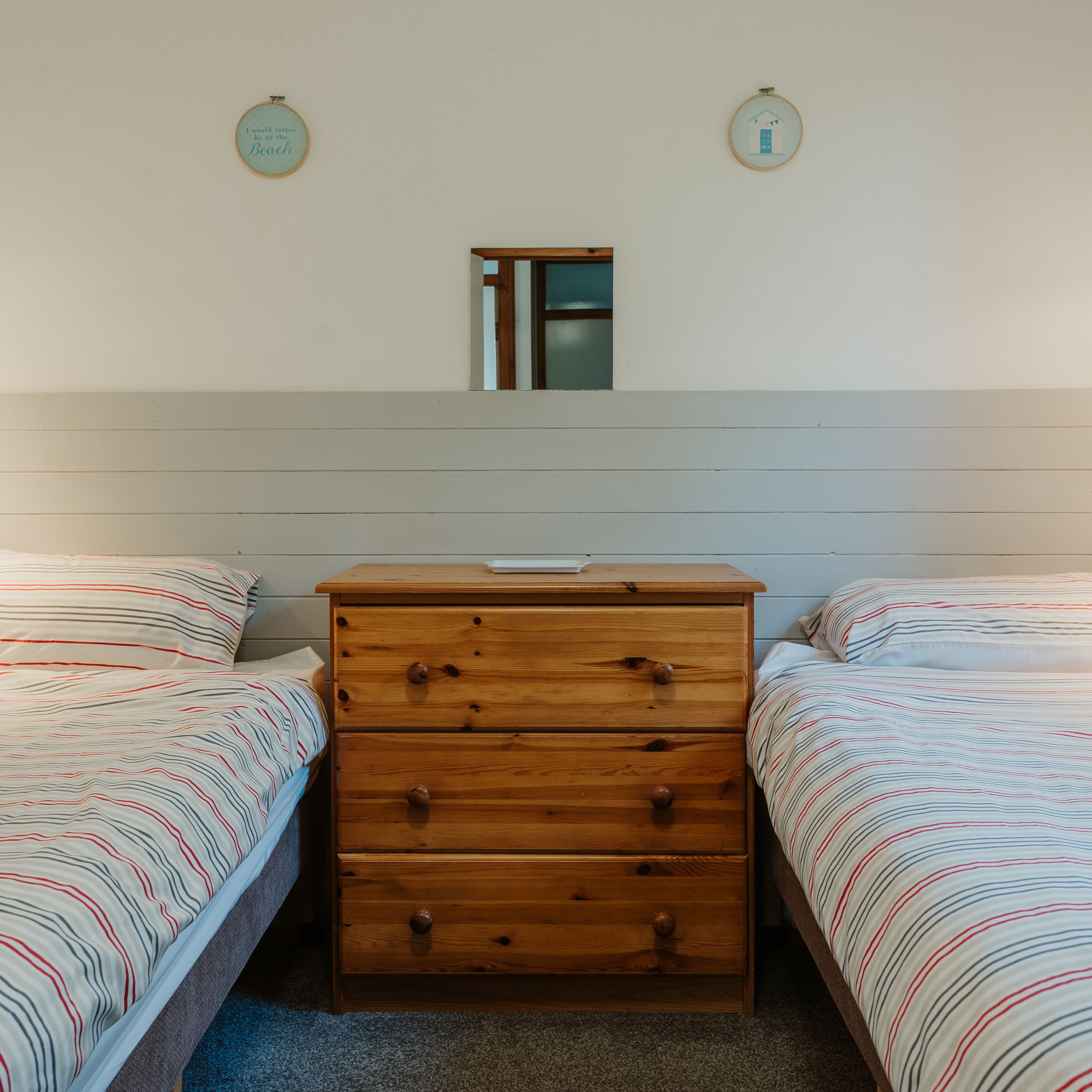 Twin bedroom with two single beds, striped bedding and a wooden chest of drawers between them