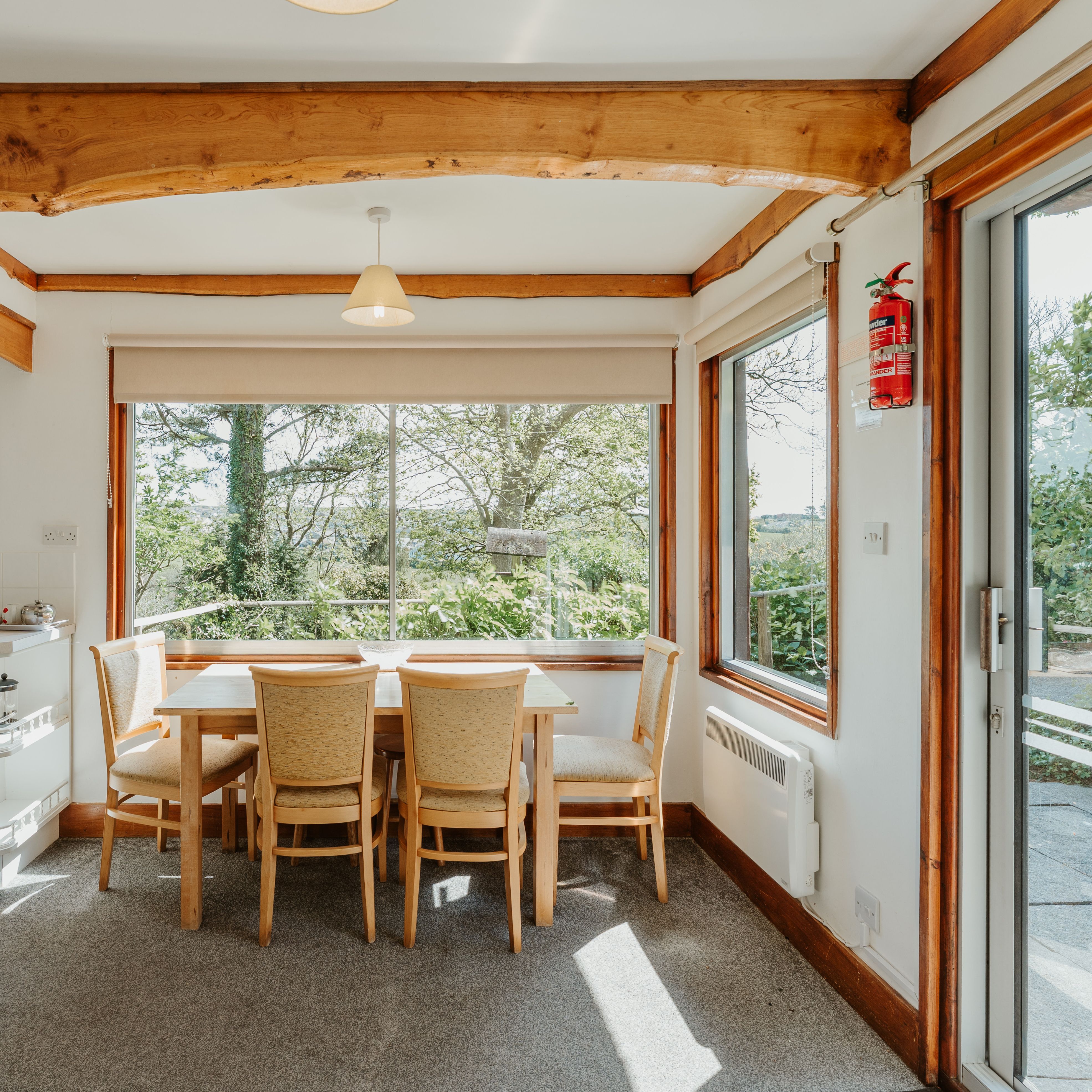 Dining area with wooden table and chairs by large window, exposed beams and garden view
