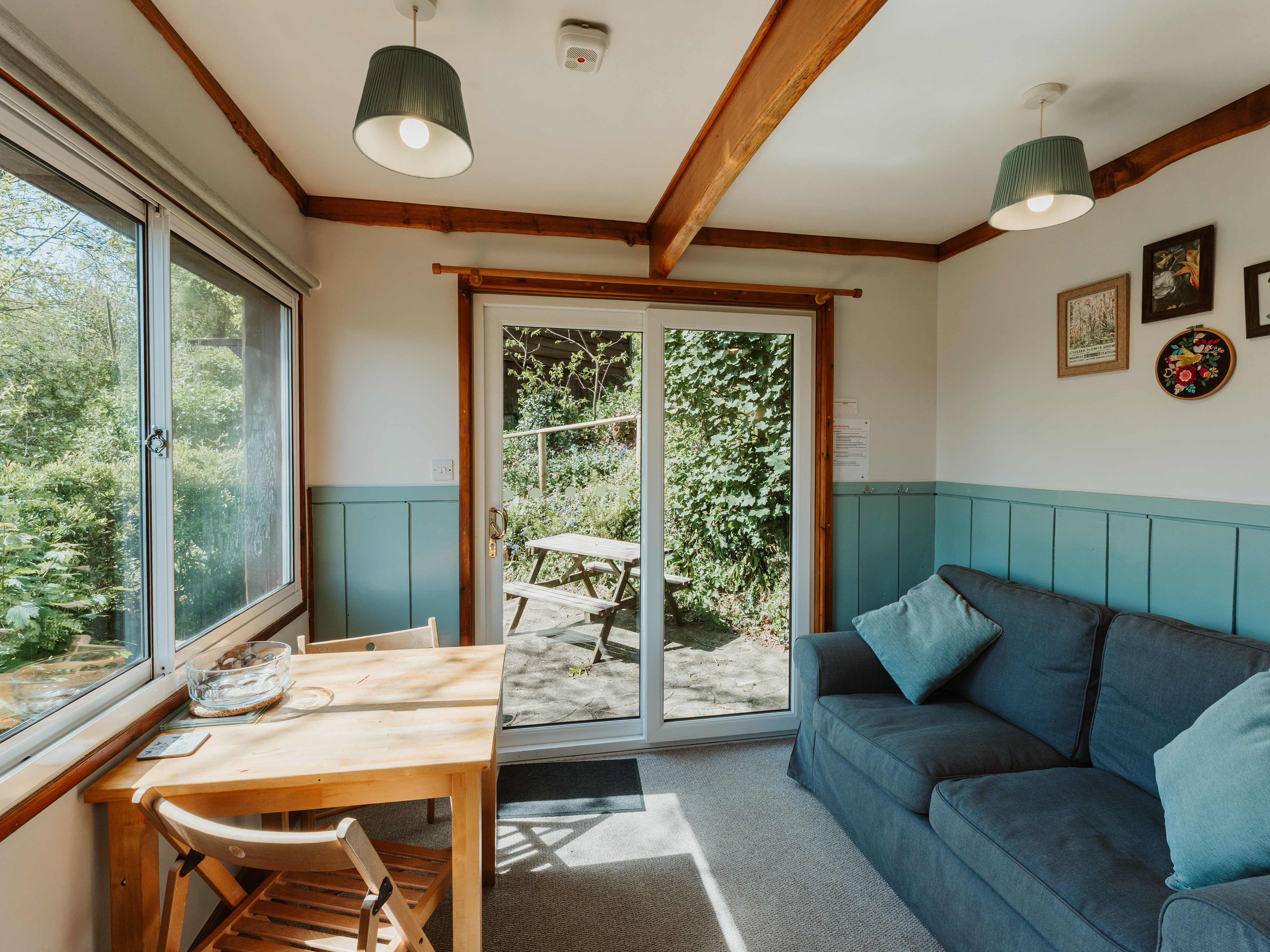Cosy living and dining area with blue sofa, wooden table and large patio doors opening to a garden terrace