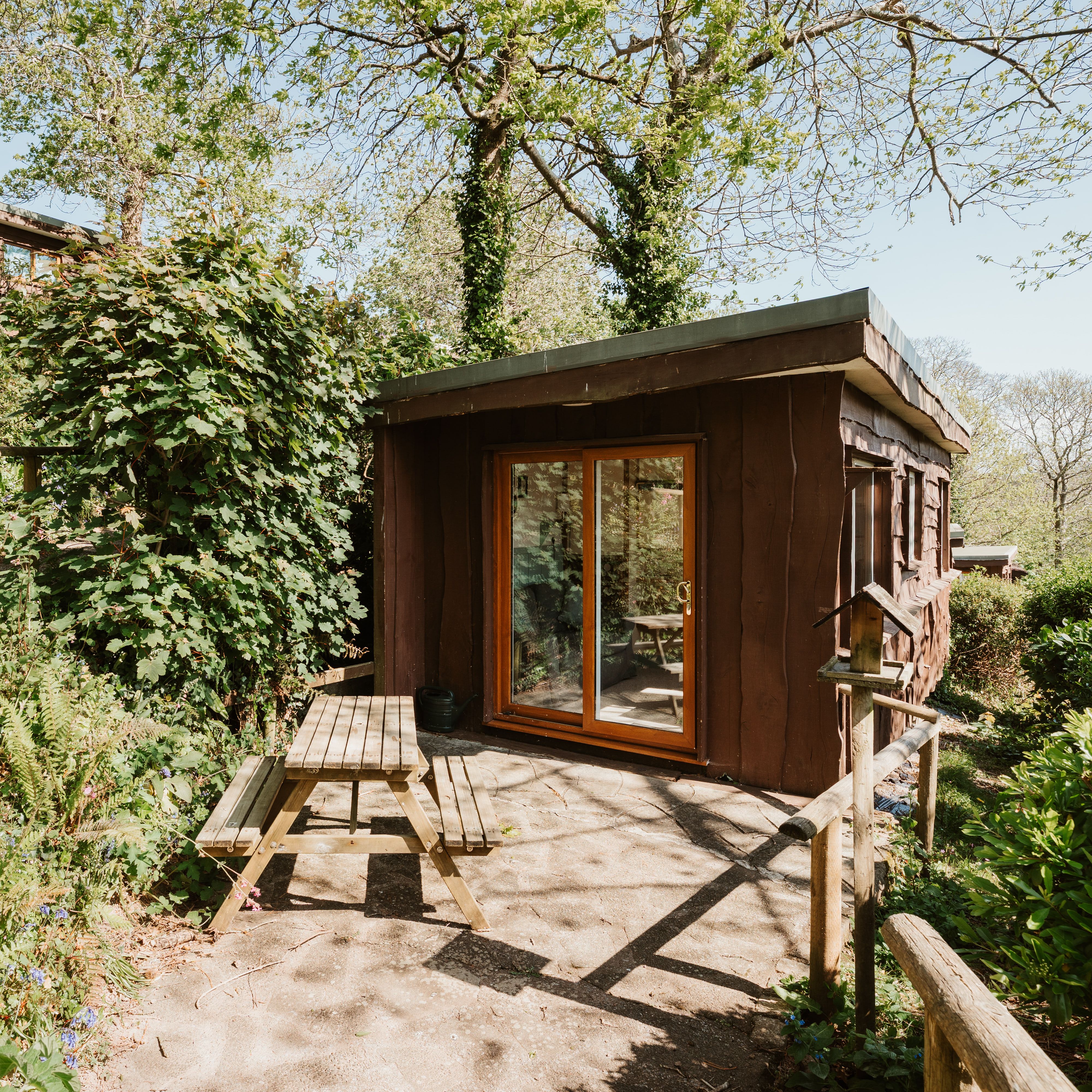 Wooden cabin with sliding glass doors and picnic bench in a leafy garden
