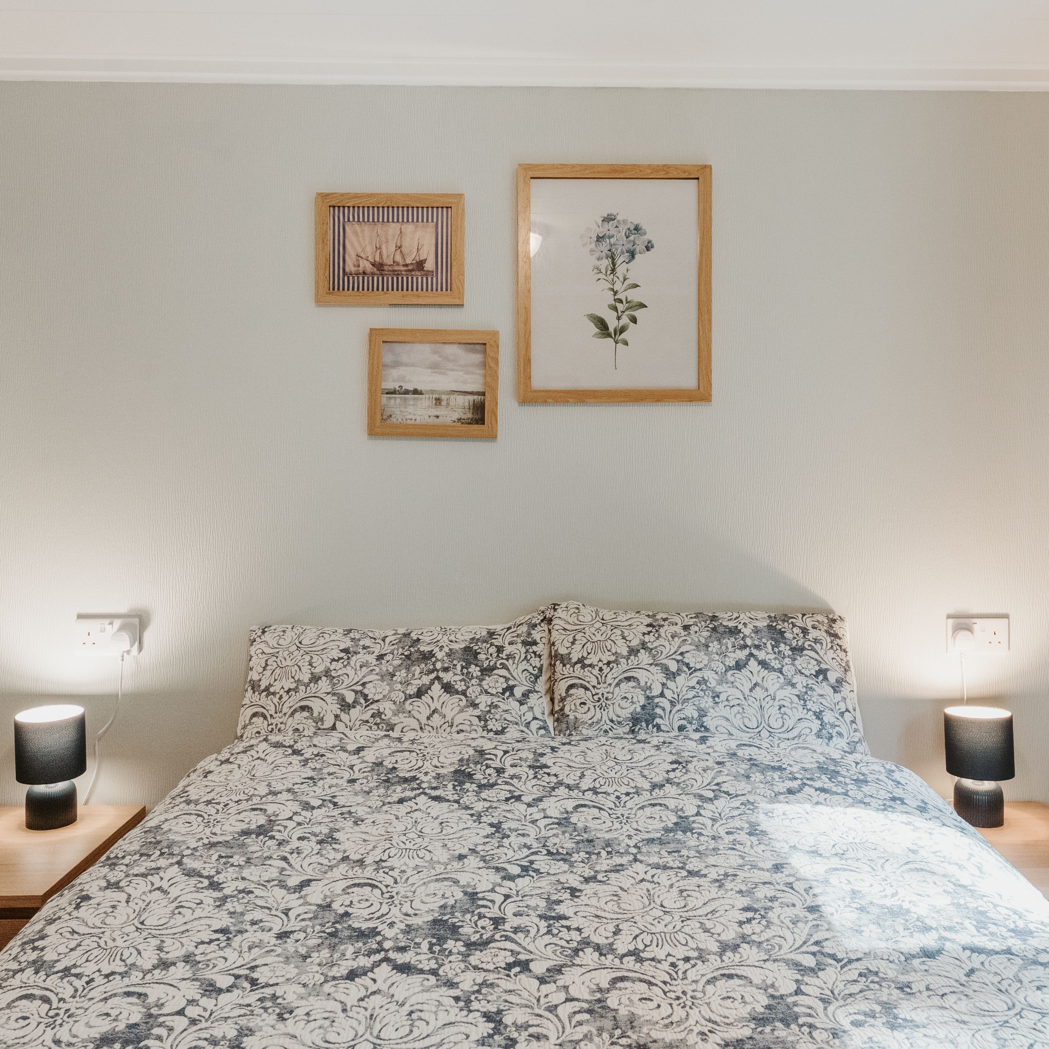 Double bed with patterned duvet, bedside lamps and framed wall art, with blue curtains