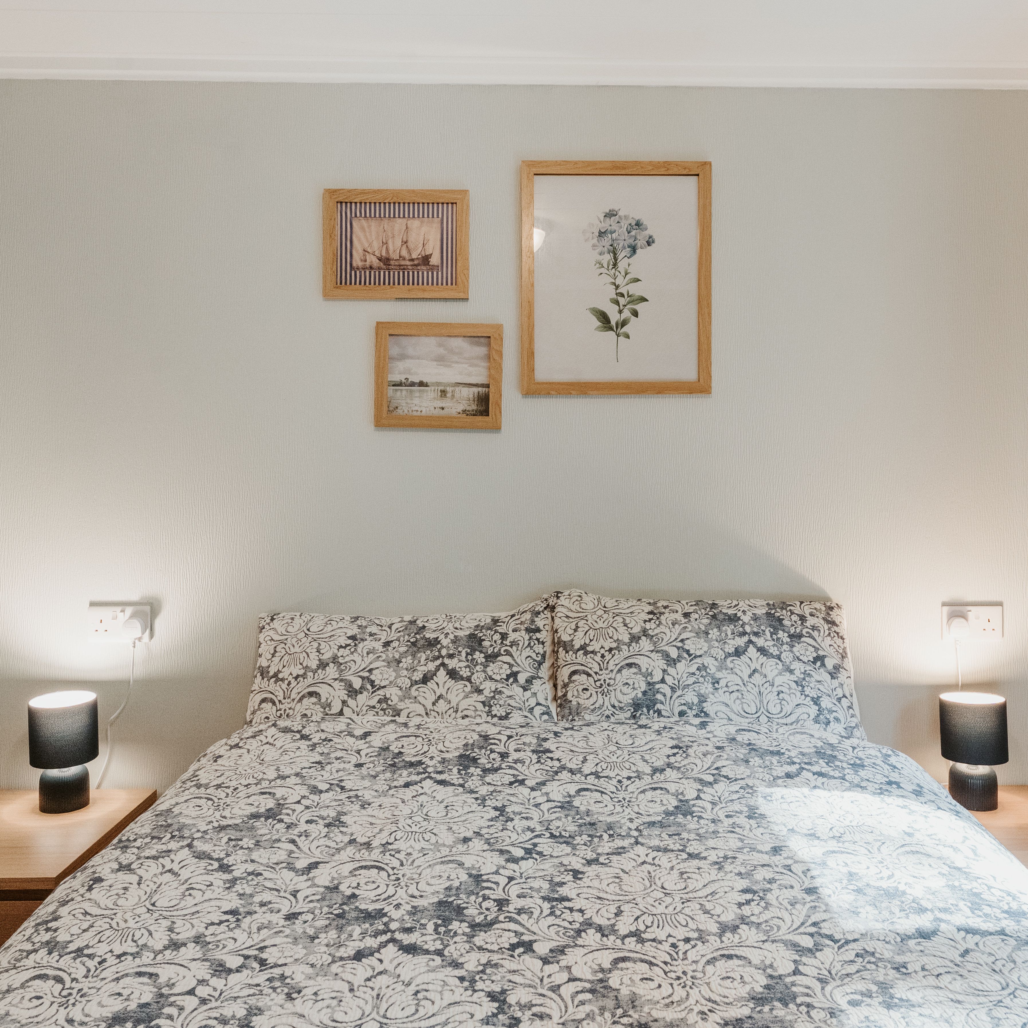 Double bed with patterned duvet, bedside lamps and framed wall art, with blue curtains