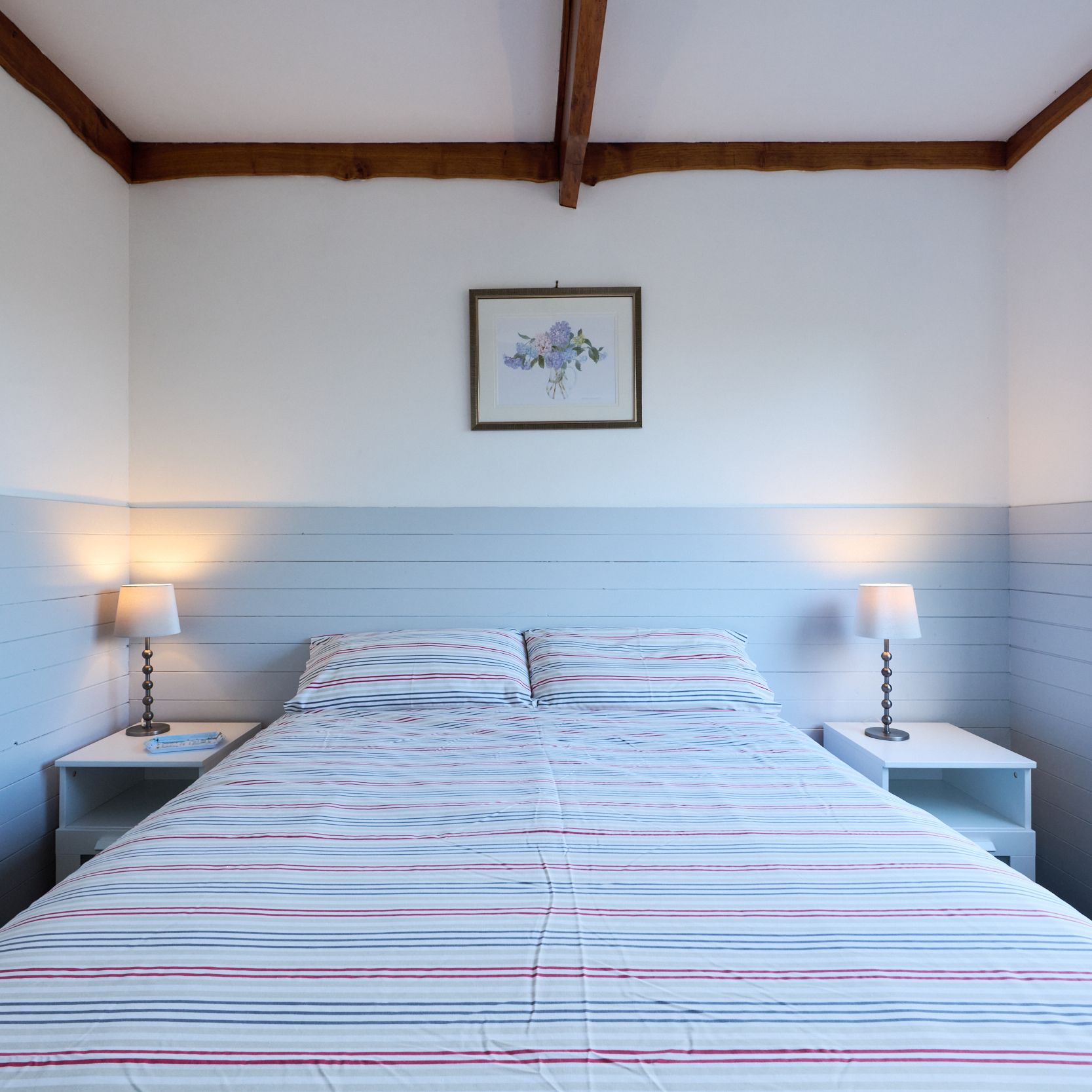 Cozy bedroom with striped bedding, two bedside tables, lamps, and a window letting in natural light.
