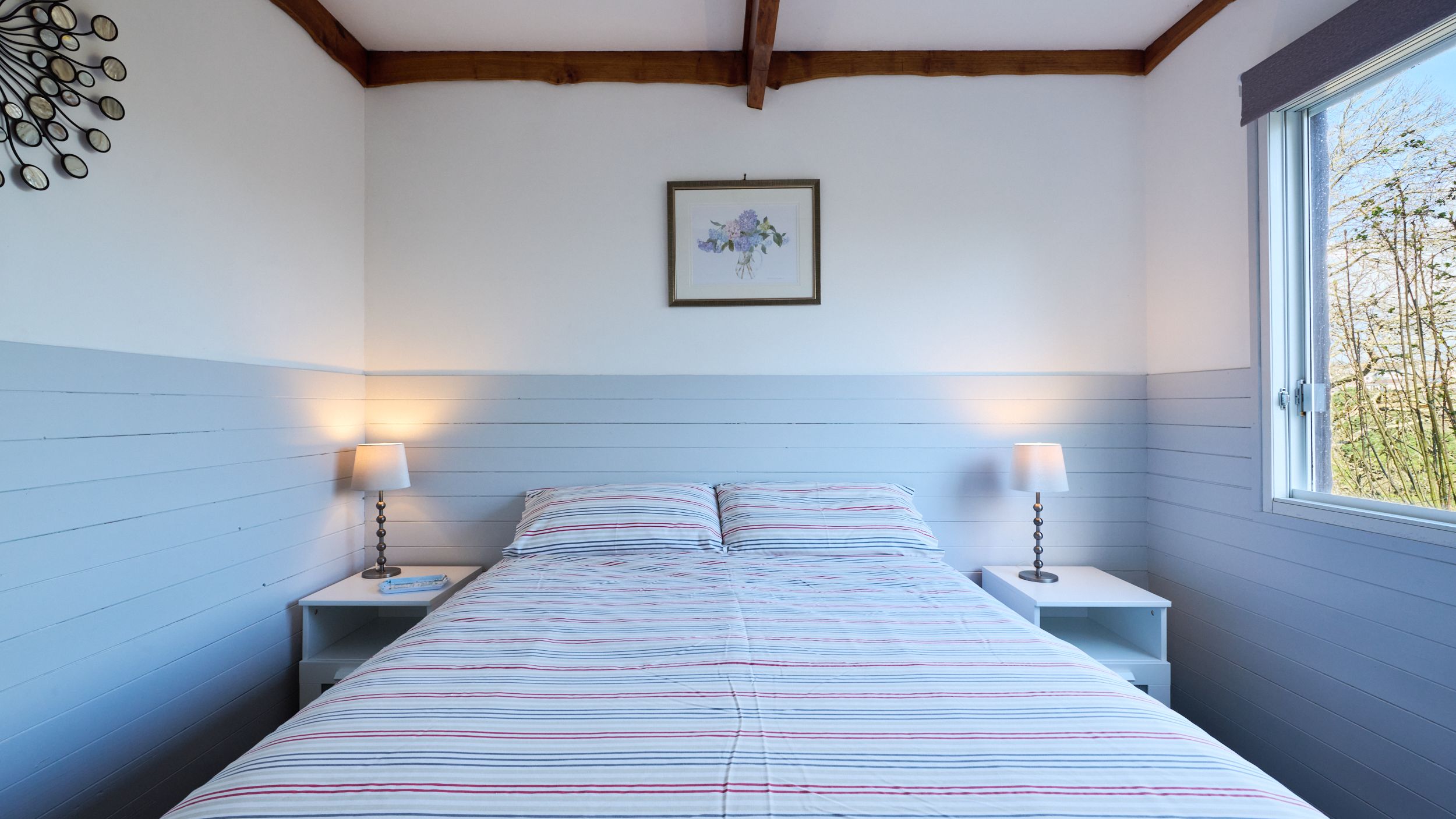 Cozy bedroom with striped bedding, two bedside tables, lamps, and a window letting in natural light.