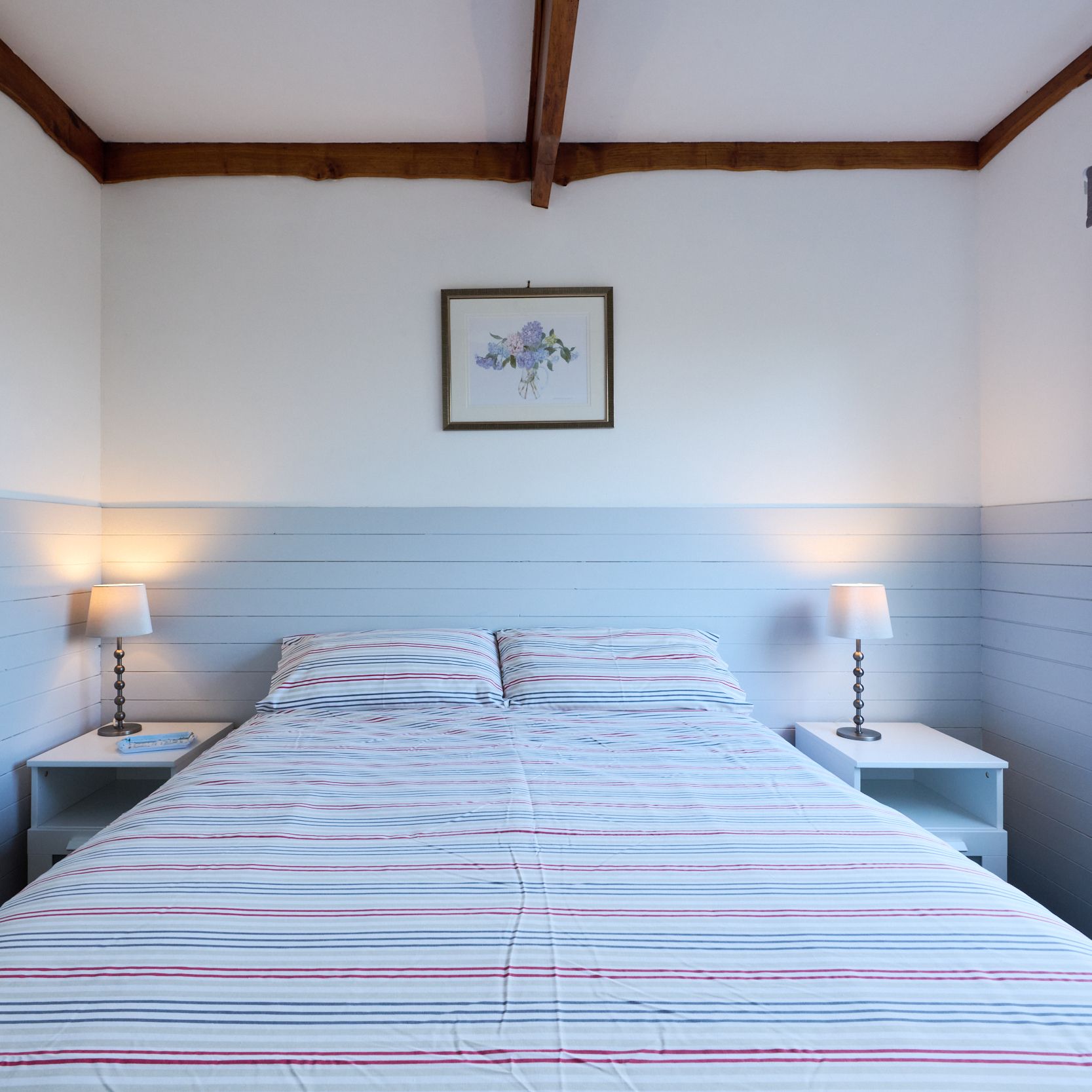 Cozy bedroom with striped bedding, two bedside tables, lamps, and a window letting in natural light.