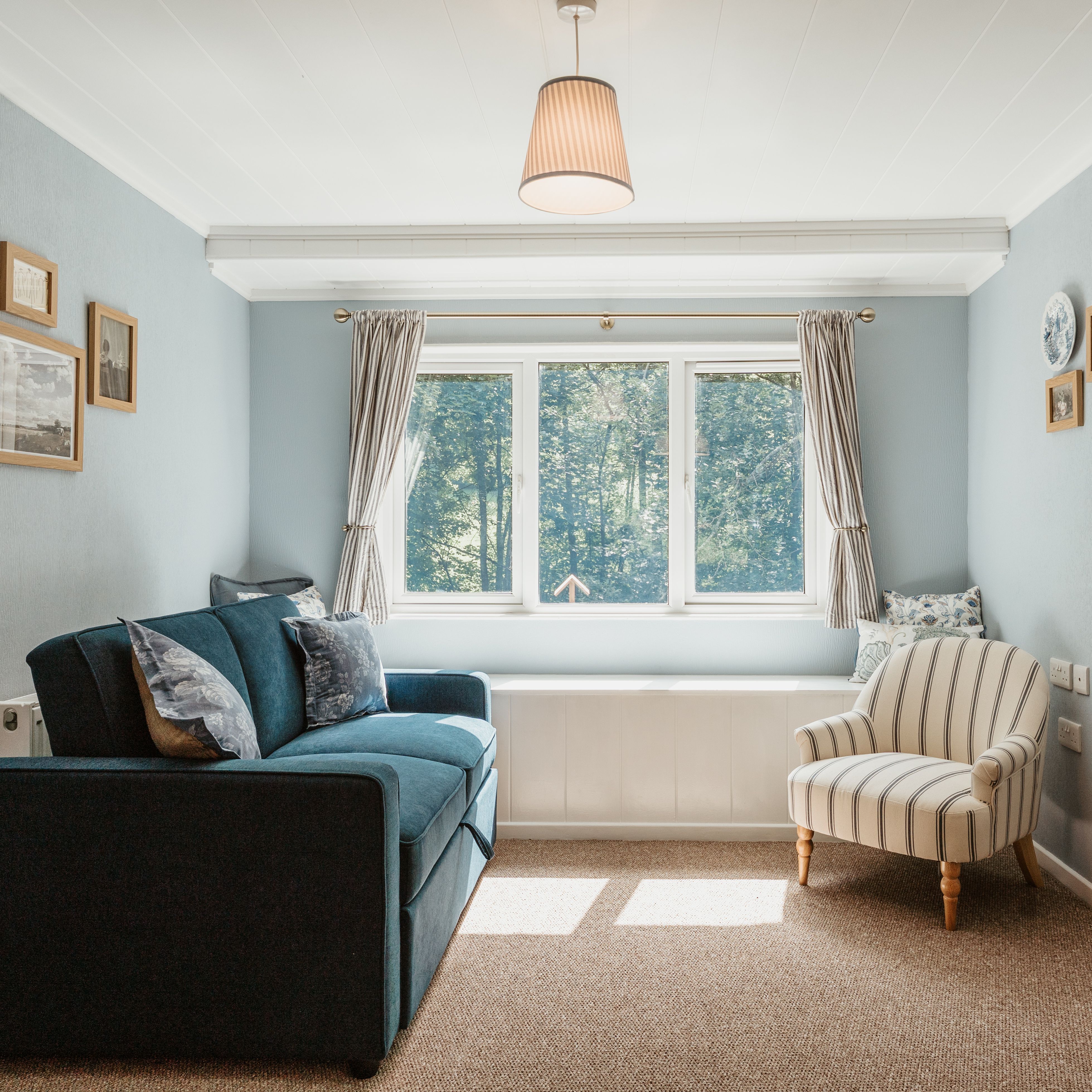 Bright sitting room with blue sofa, striped armchair and large window with curtains