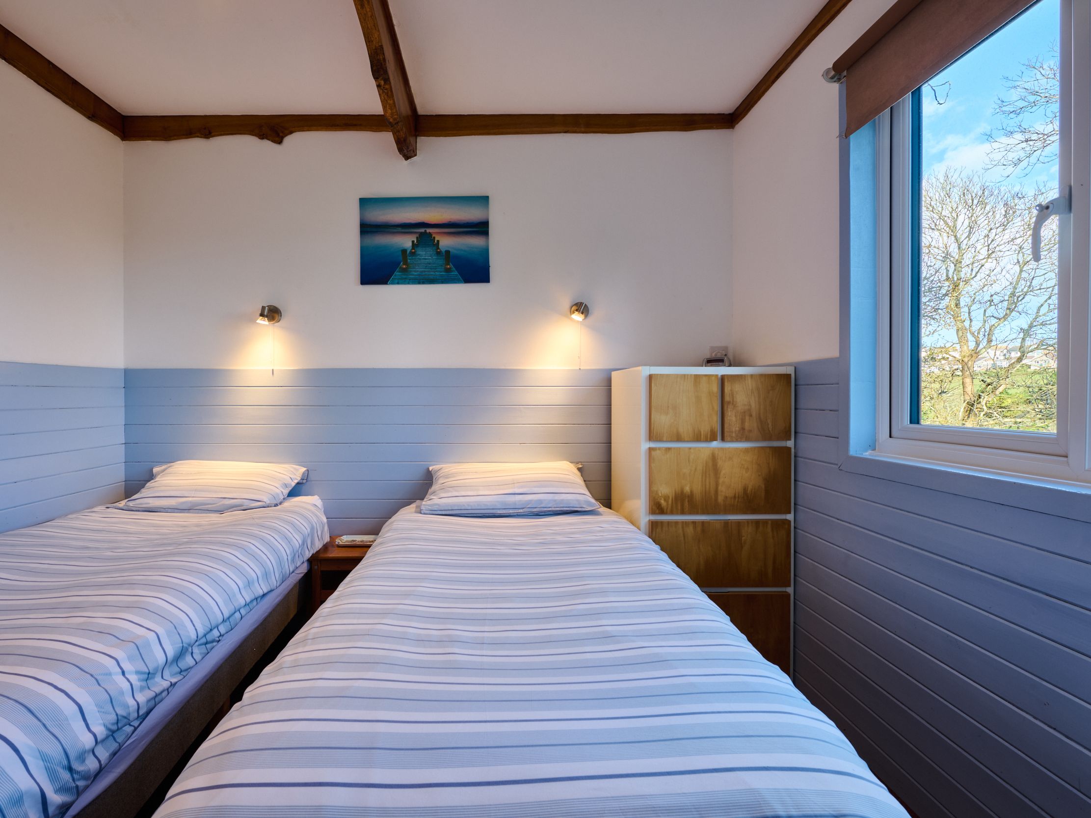 Twin bedroom with two single beds, striped bedding, a window, and a painting of a dock over water on the wall.