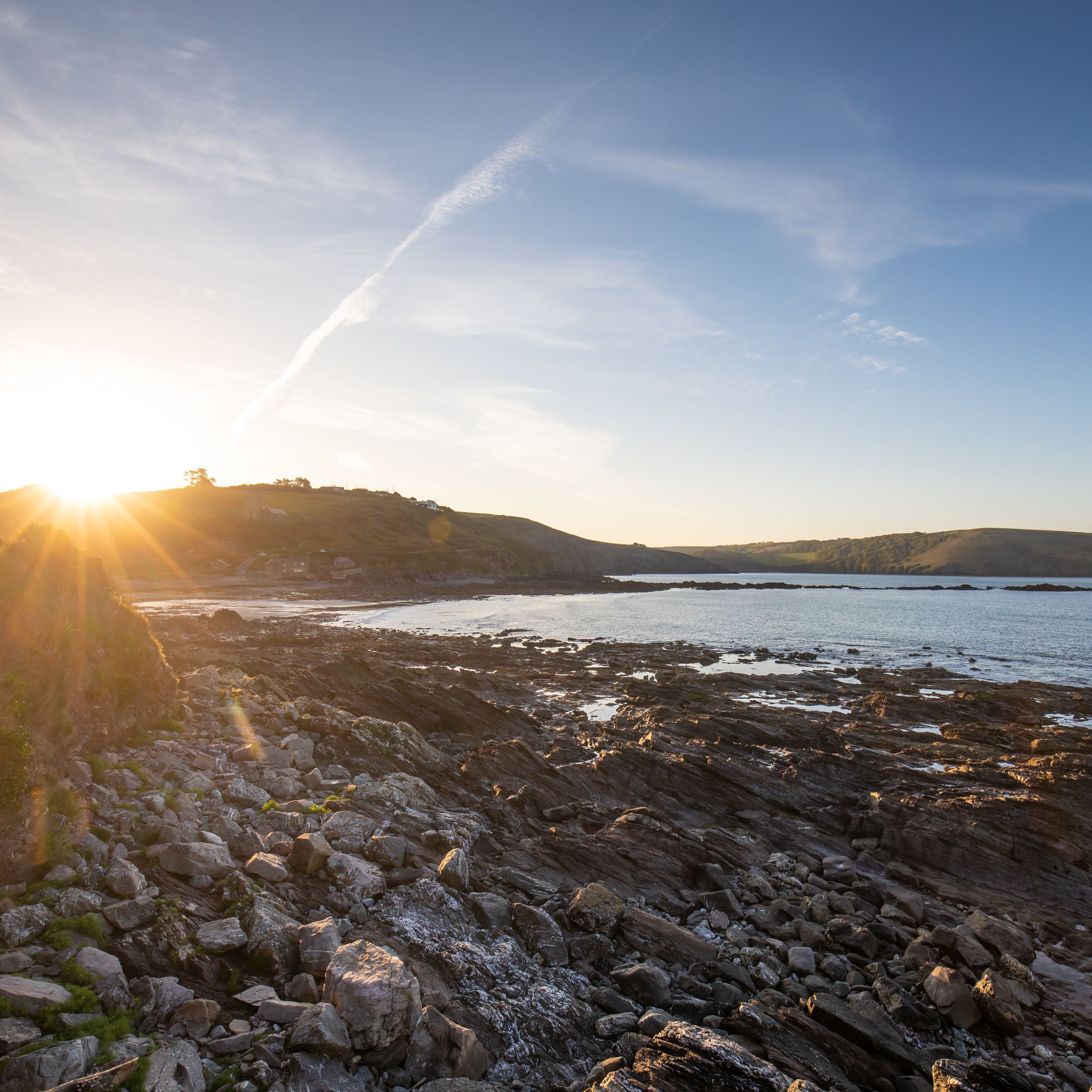 Sunset over a rocky coastline with calm sea and distant hills