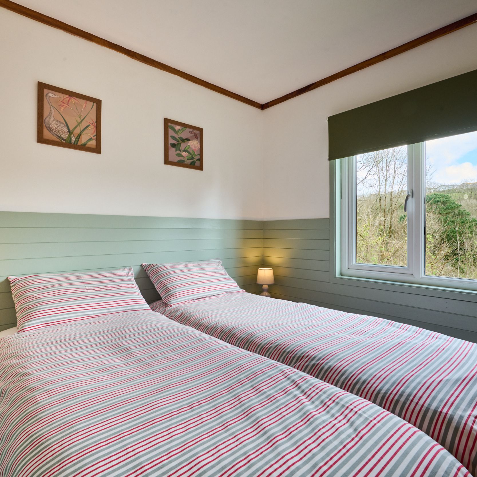 Cozy twin bedroom with striped bedding, soft lighting and a window view of greenery.