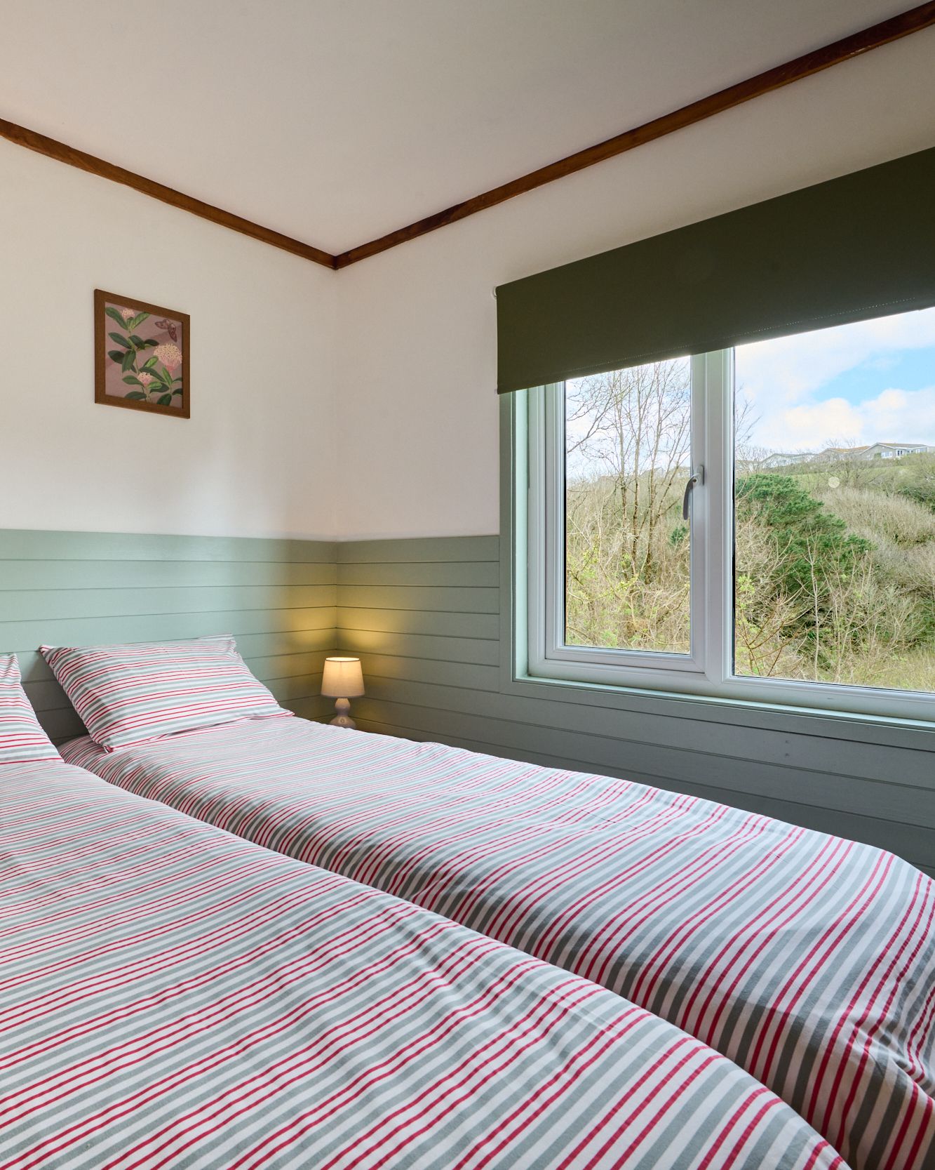 Cozy twin bedroom with striped bedding, soft lighting and a window view of greenery.