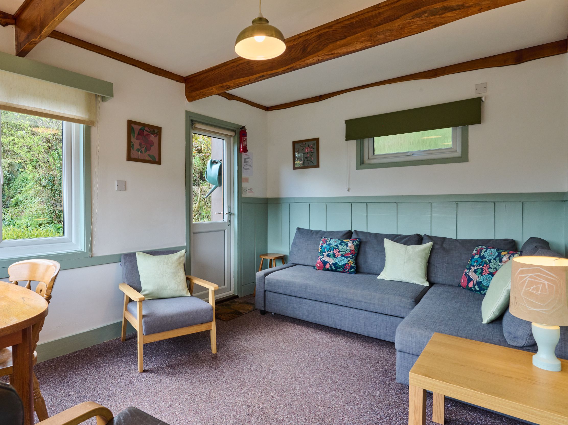Cozy living room with gray sofa, floral cushions, armchair, and wooden beams.