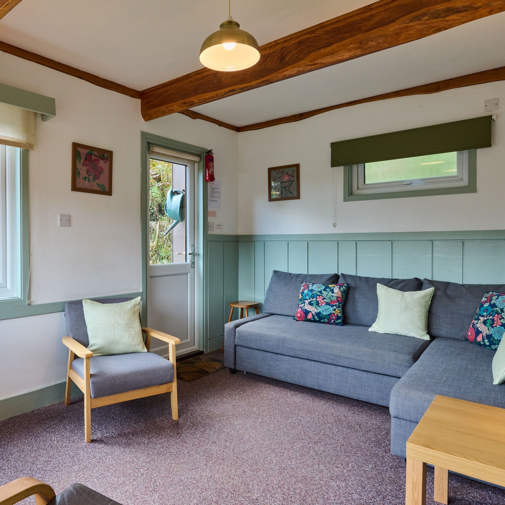 Cozy living room with gray sofa, floral cushions, armchair, and wooden beams.