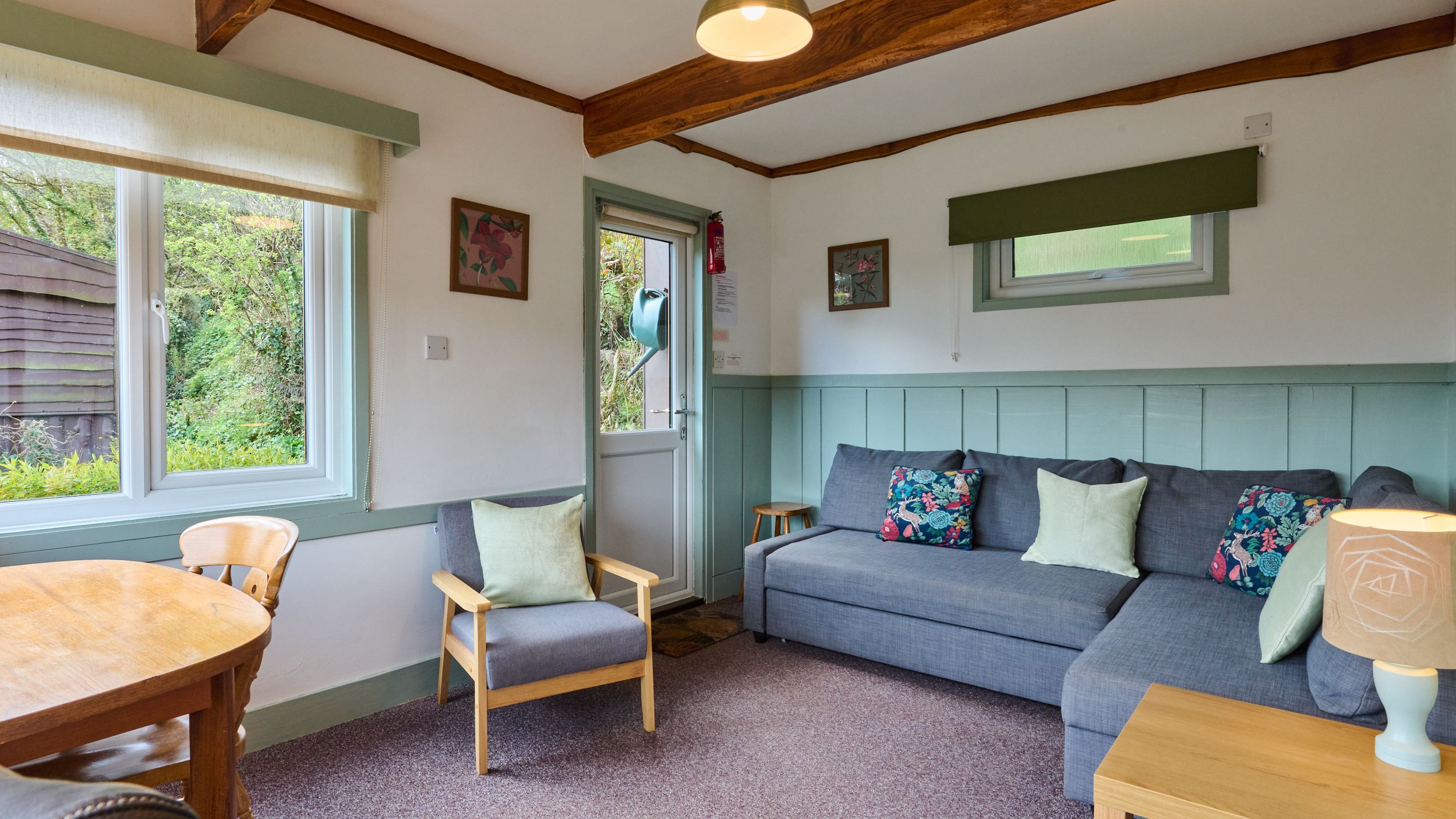 Cozy living room with gray sofa, floral cushions, armchair, and wooden beams.
