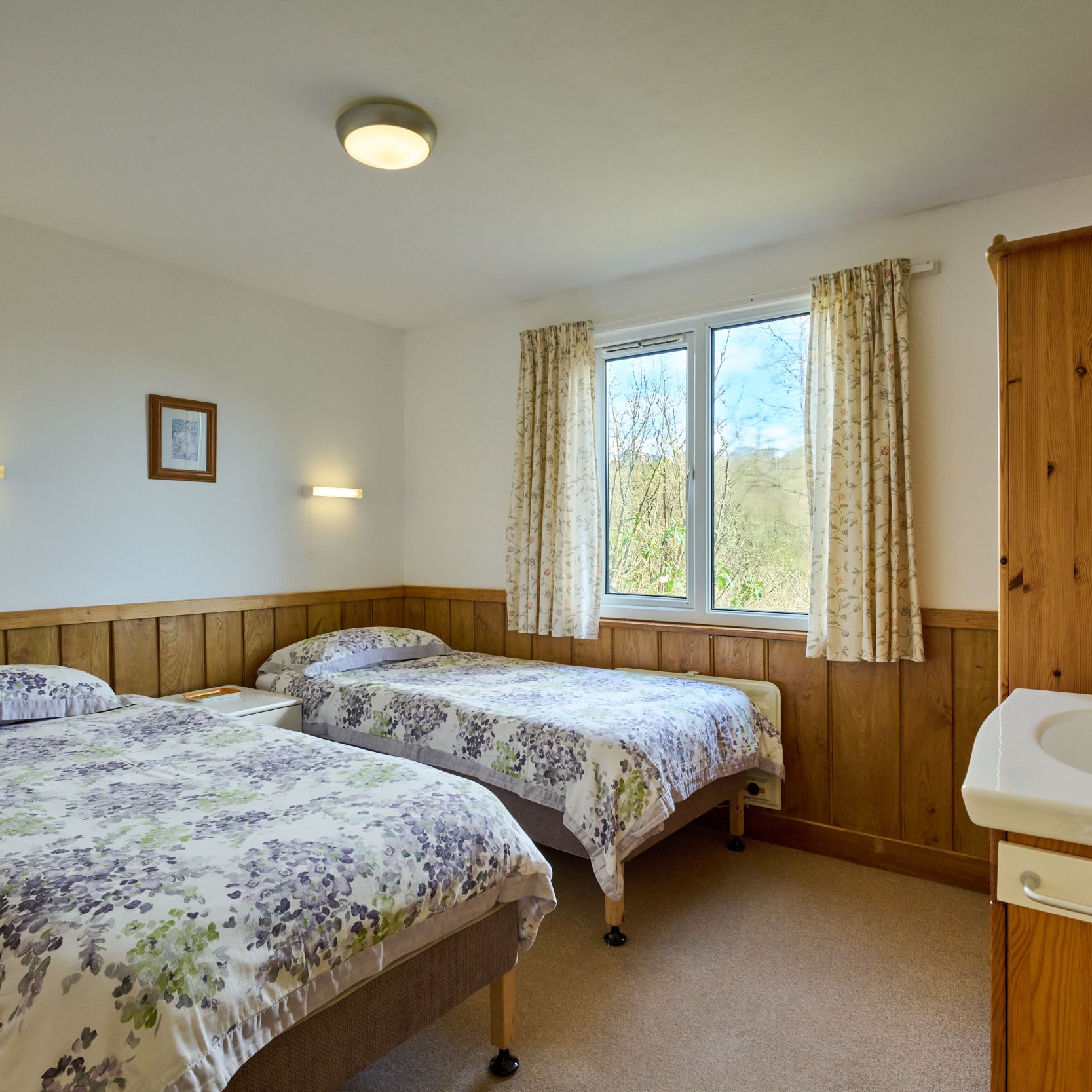 Cozy twin bedroom with floral bedding, wooden furniture, and window view