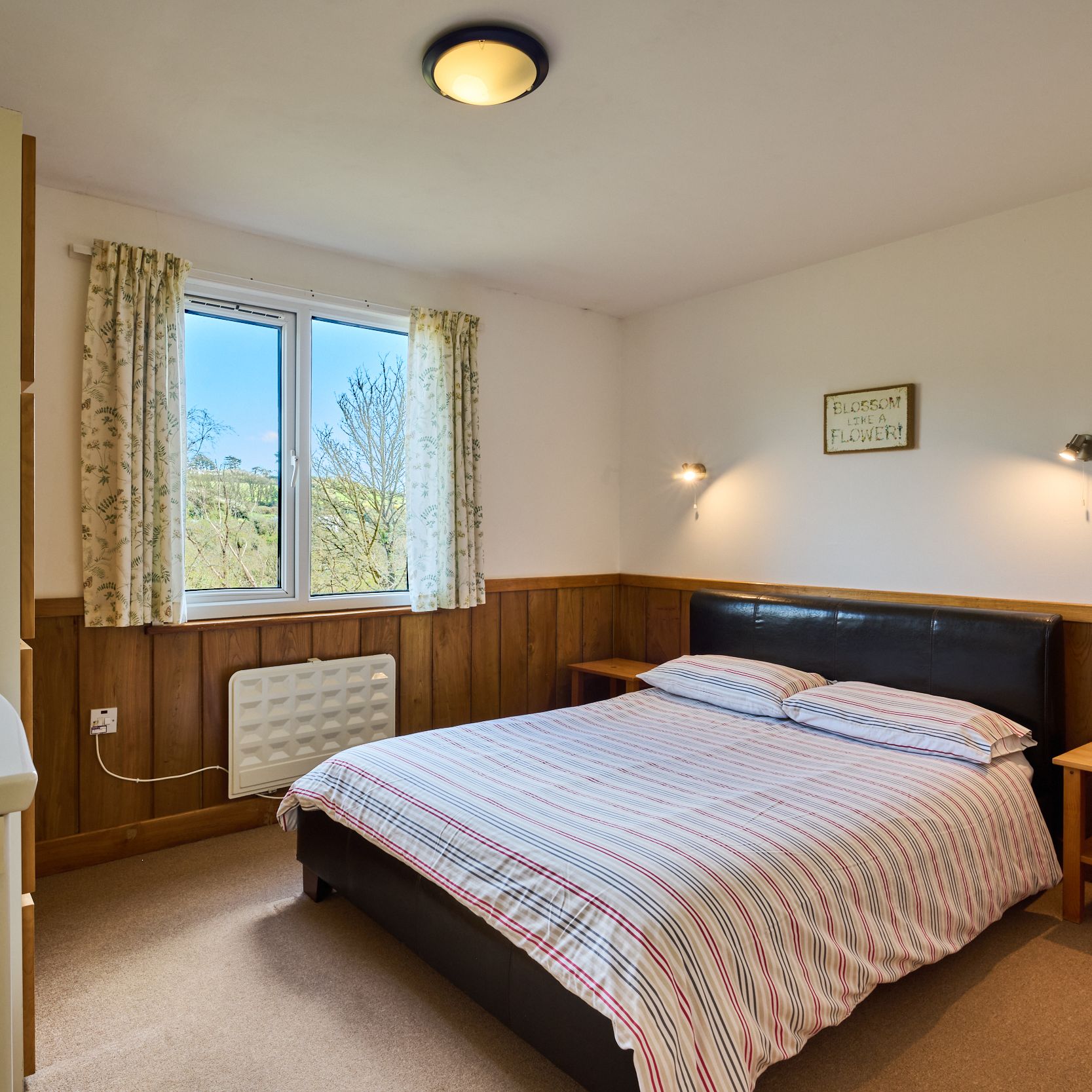 Cozy bedroom with a double bed, wooden accents, and a window overlooking greenery.