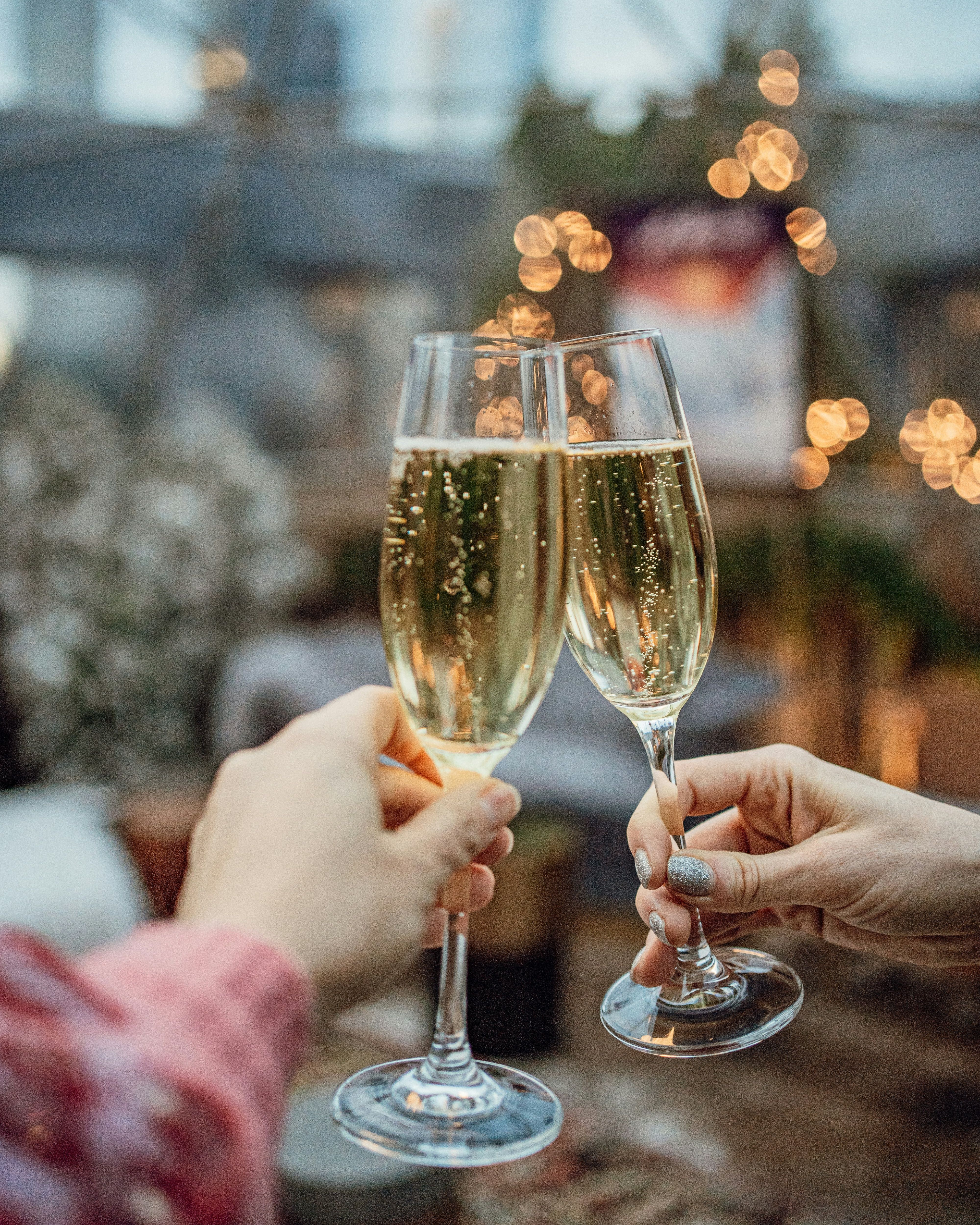 Two people clinking champagne glasses with a blurred festive background