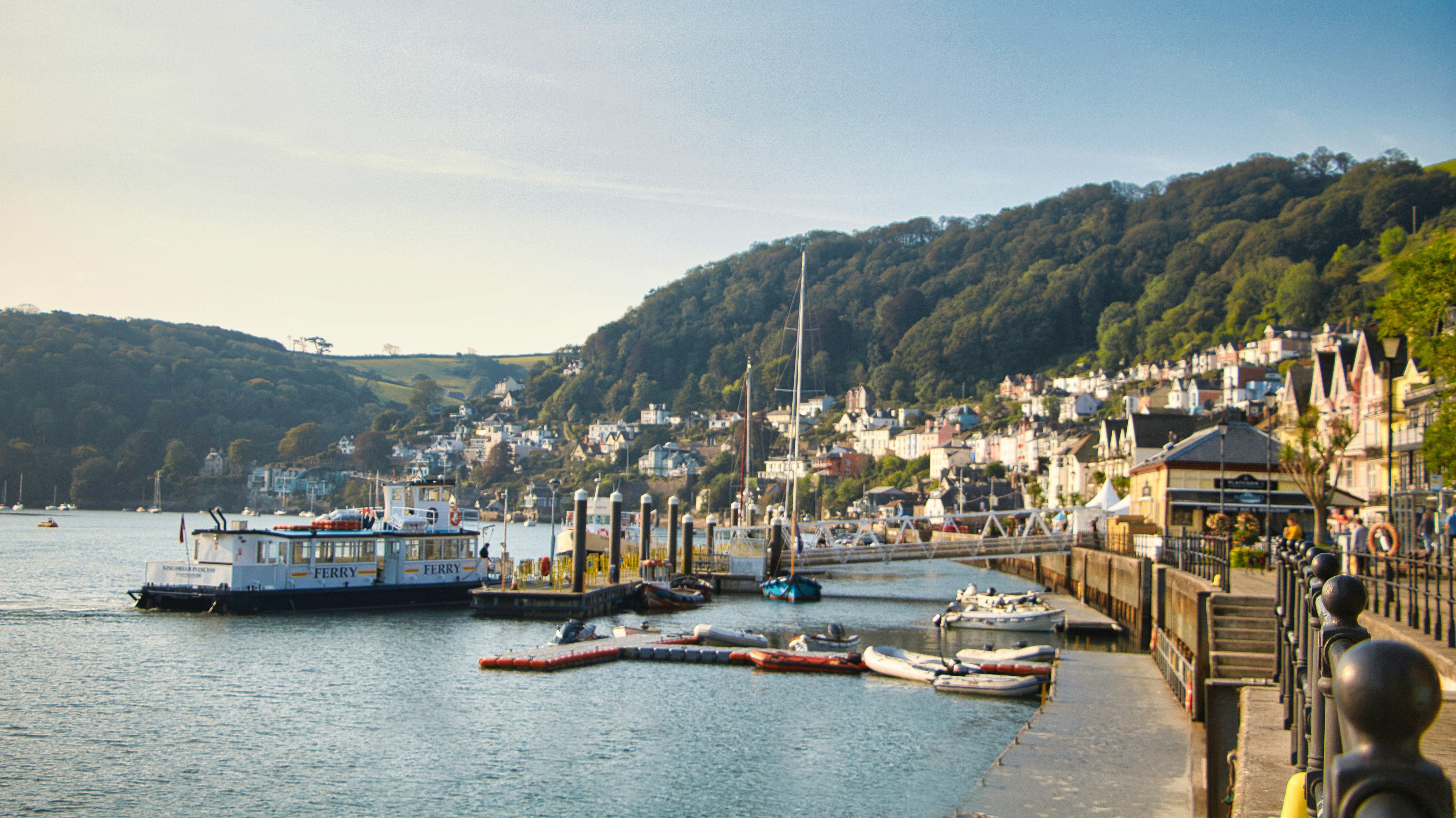 A picturesque harbor with a ferry, small boats, and waterfront houses nestled on a hillside.