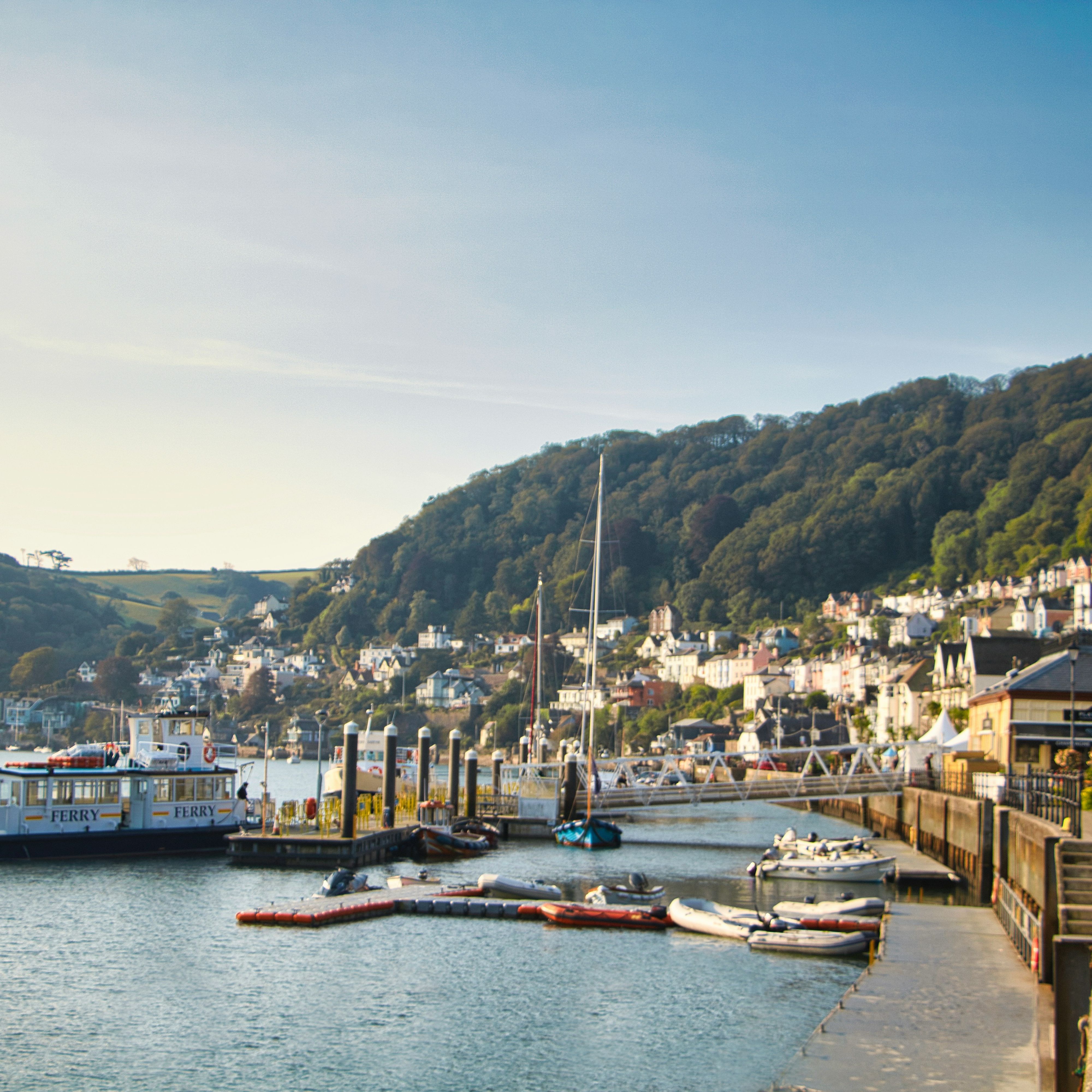A picturesque harbor with a ferry, small boats, and waterfront houses nestled on a hillside.