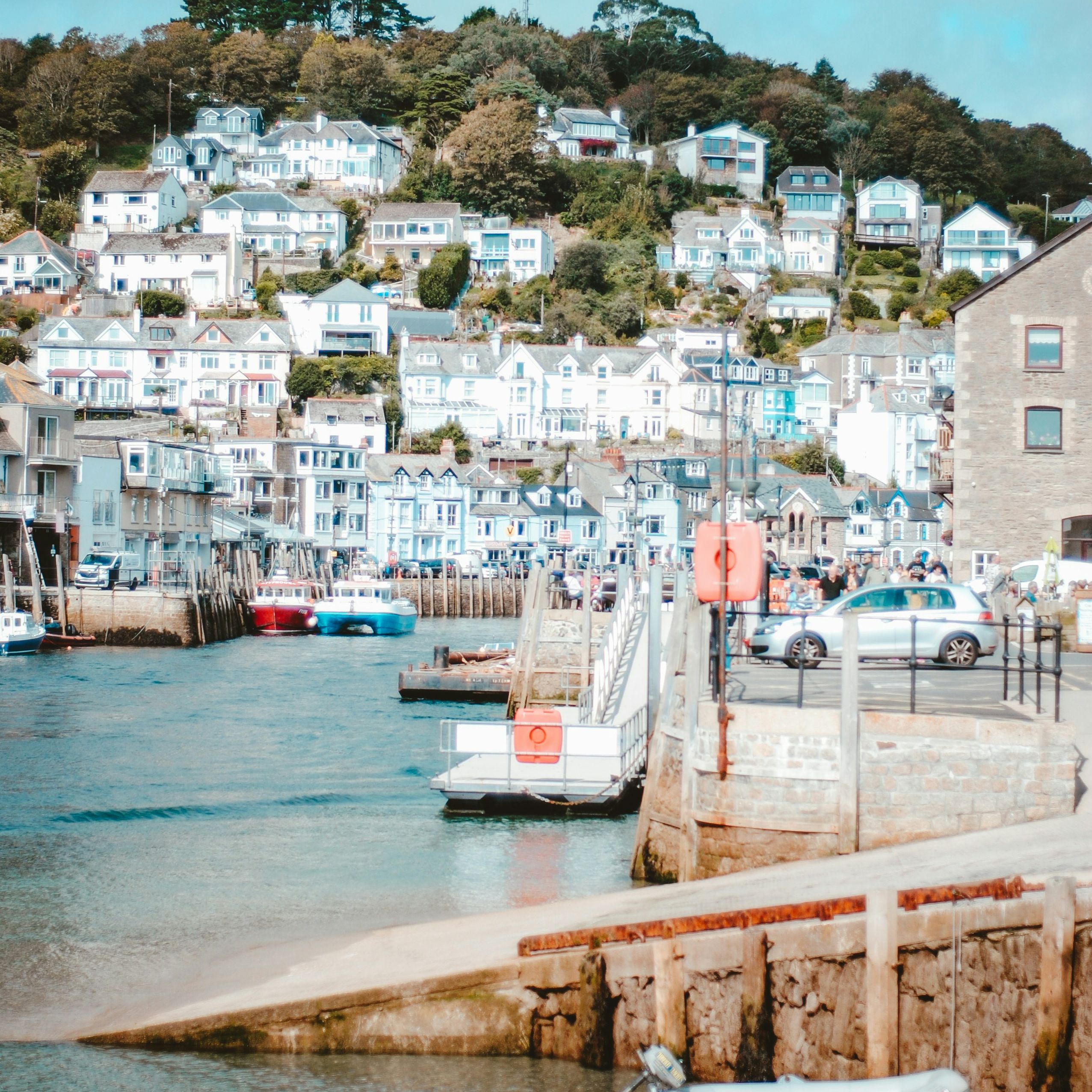 Coastal village with colorful houses on a hillside and boats docked by the waterfront.