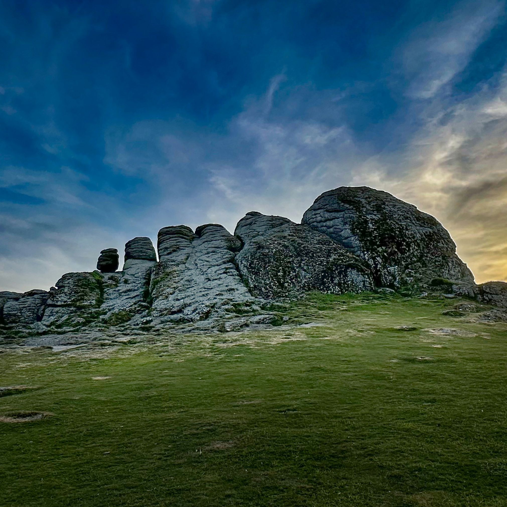 Large rocky outcrop on grassy field under a dramatic sky at sunset