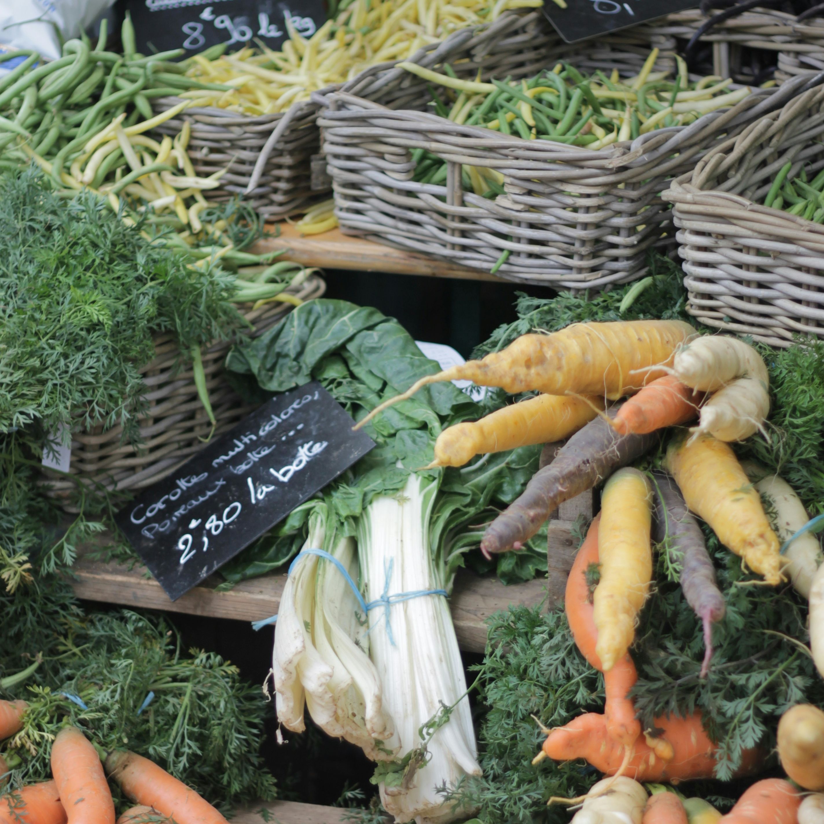 A market stall displaying a variety of fresh vegetables including multicolored carrots, green beans, and leafy greens.