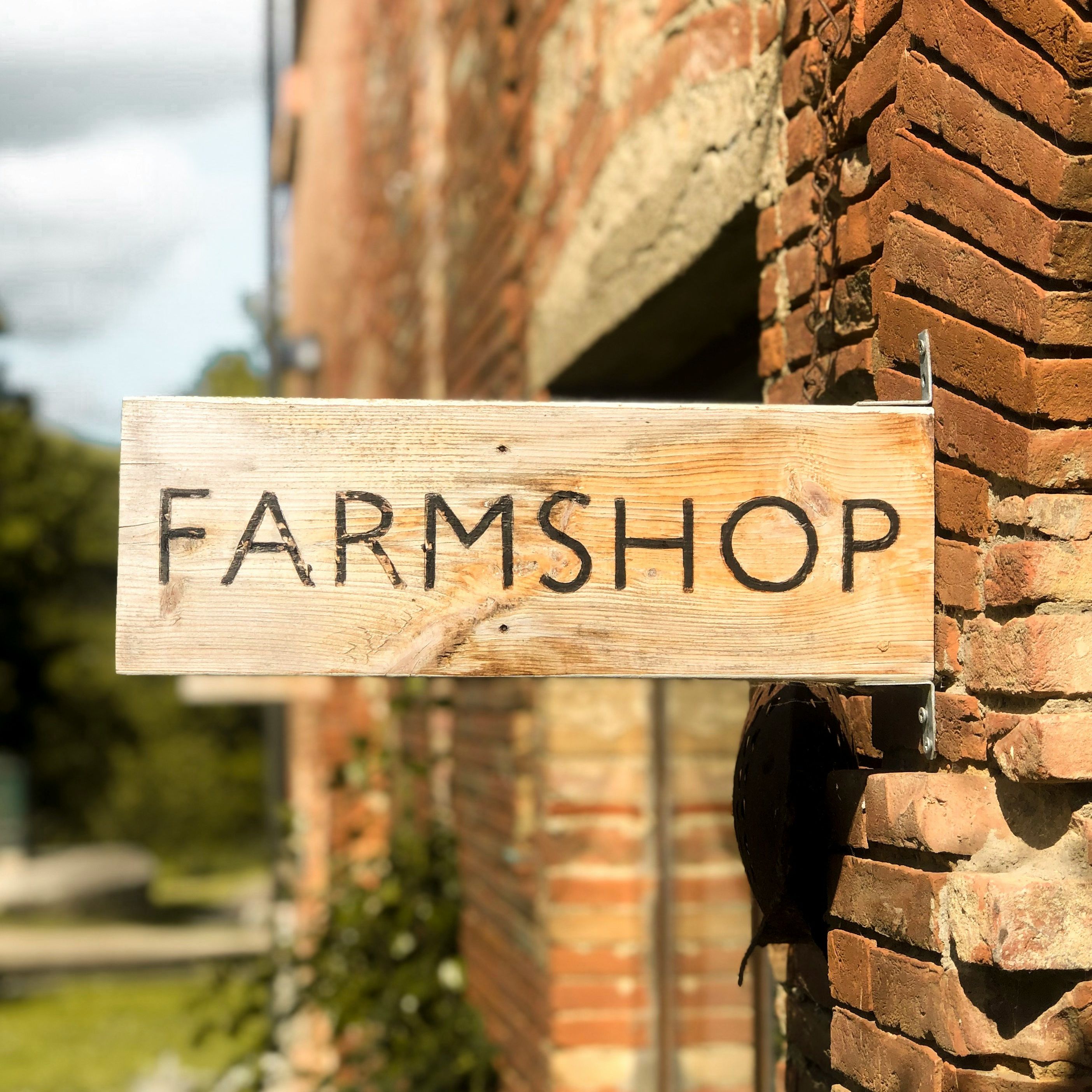 Wooden farm shop sign attached to a brick wall