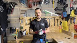 Person sitting in a workshop surrounded by various tools mounted on the walls and placed on the workbench.