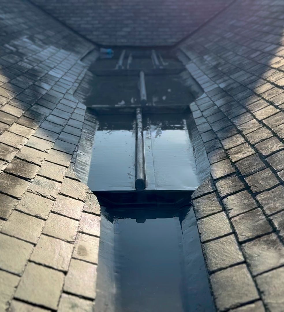 Close-up view of a slate tiled roof valley with metal flashing and standing water