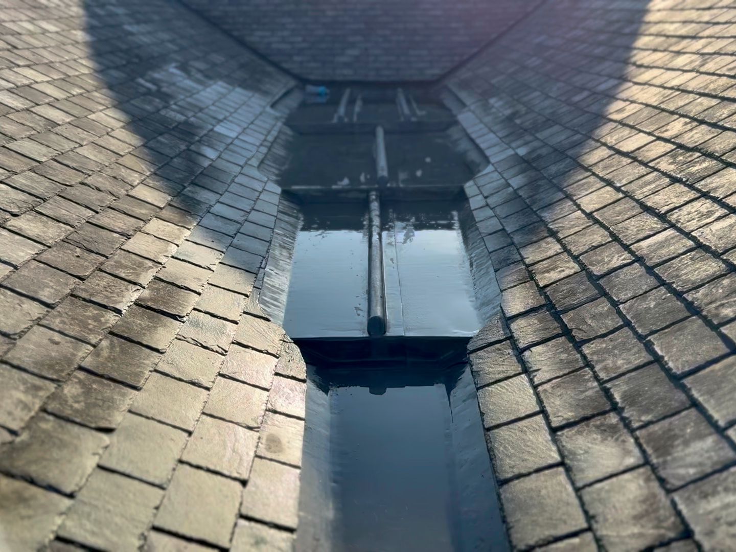Close-up view of a slate tiled roof valley with metal flashing and standing water