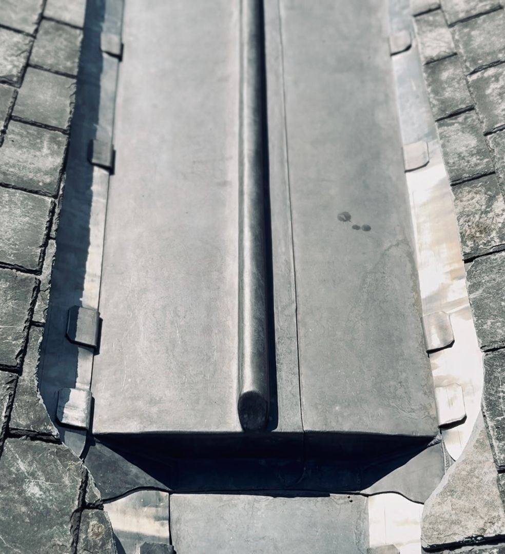 Close-up of slate roof tiles with metal flashing along a roof valley.